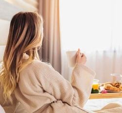 Woman in bathrobe enjoying coffee and breakfast in bed