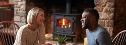 Couple smiling and enjoying coffee together by a fireplace in a cozy rustic setting
