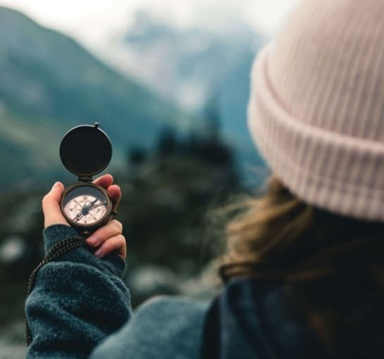 Person holding a compass outdoors with mountains in the background