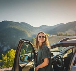 Woman standing by car with mountains in the background