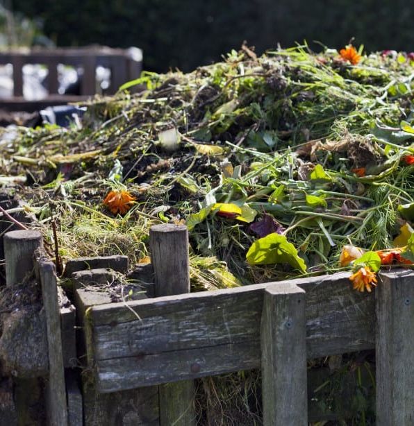 A compost heap made of garden waste and food scraps in a wooden bin outdoors.
