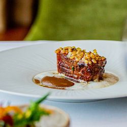 Gourmet beef dish topped with grains on a white plate, garnished with sauce