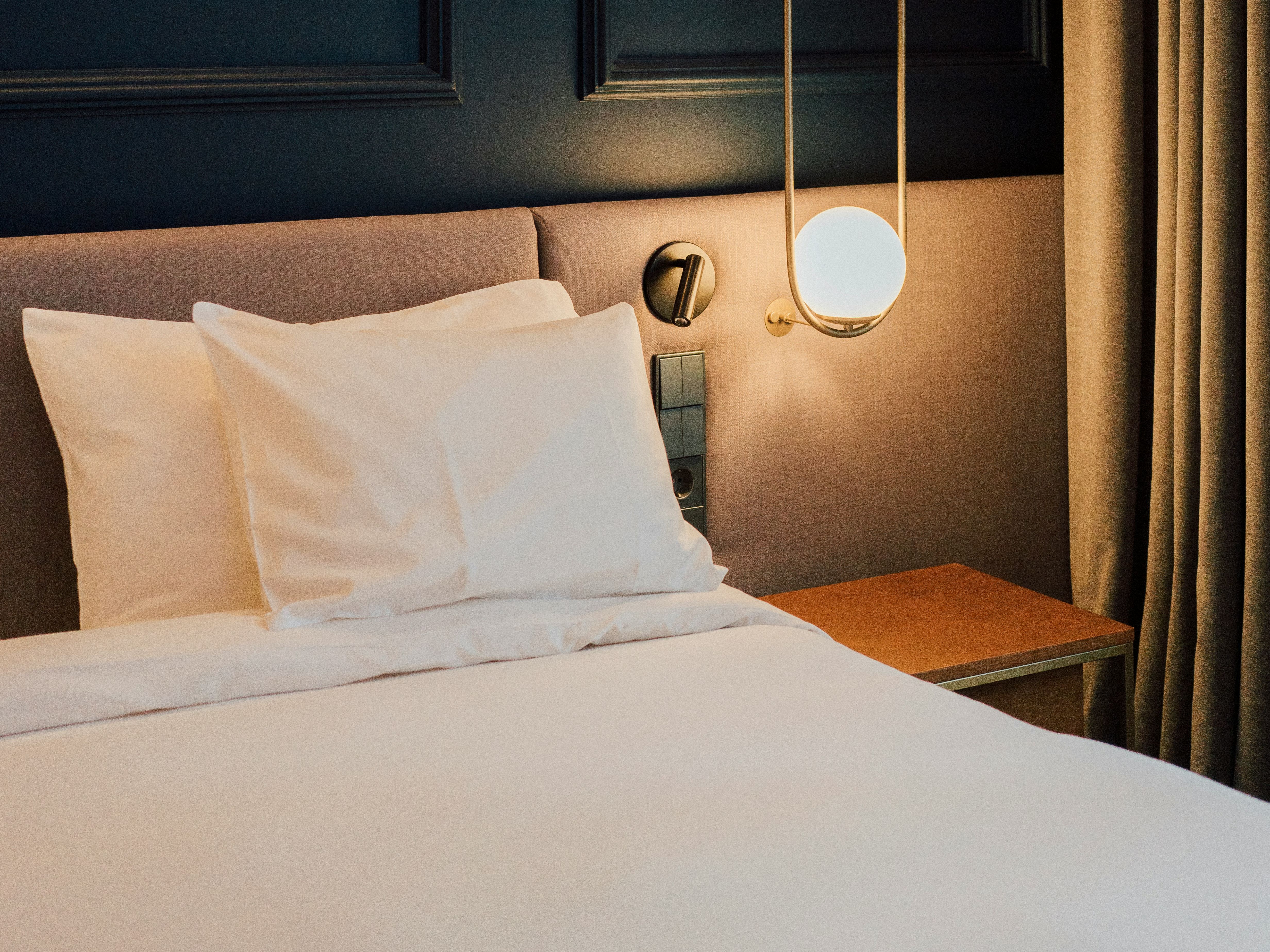 Modern hotel room with neatly made bed, white linens, and a contemporary hanging bedside lamp