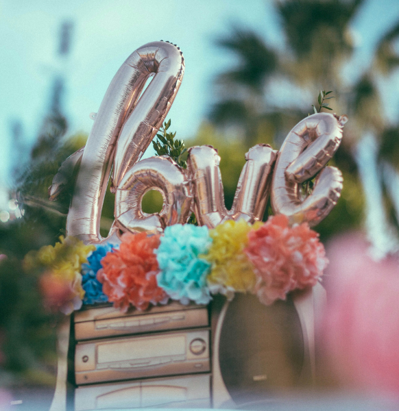 Metallic 'love' letter balloons with colorful paper flowers and a decorative radio outdoors
