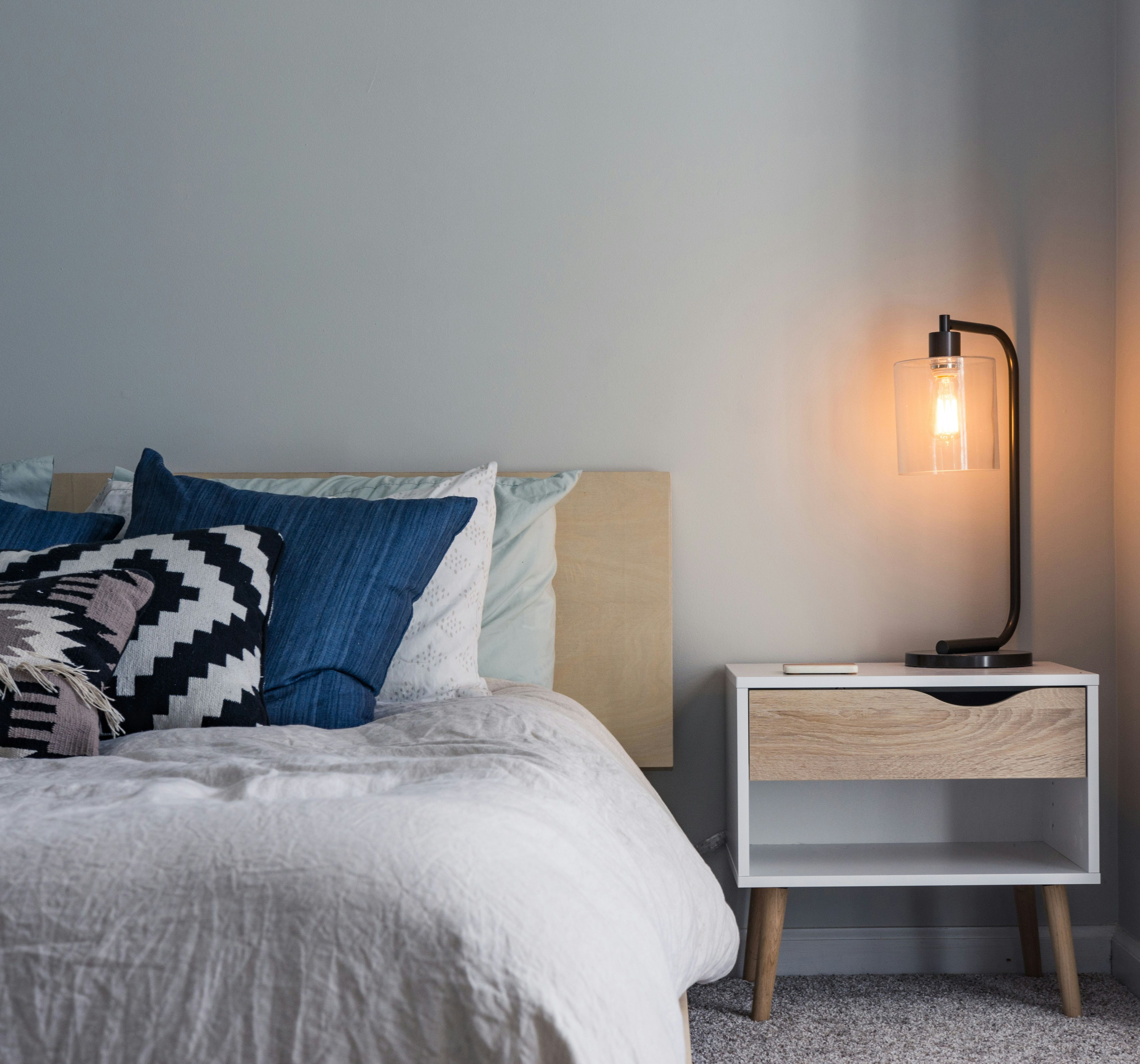 Modern bedroom with blue and white bedding, a geometric pillow, and a lit bedside lamp on a nightstand