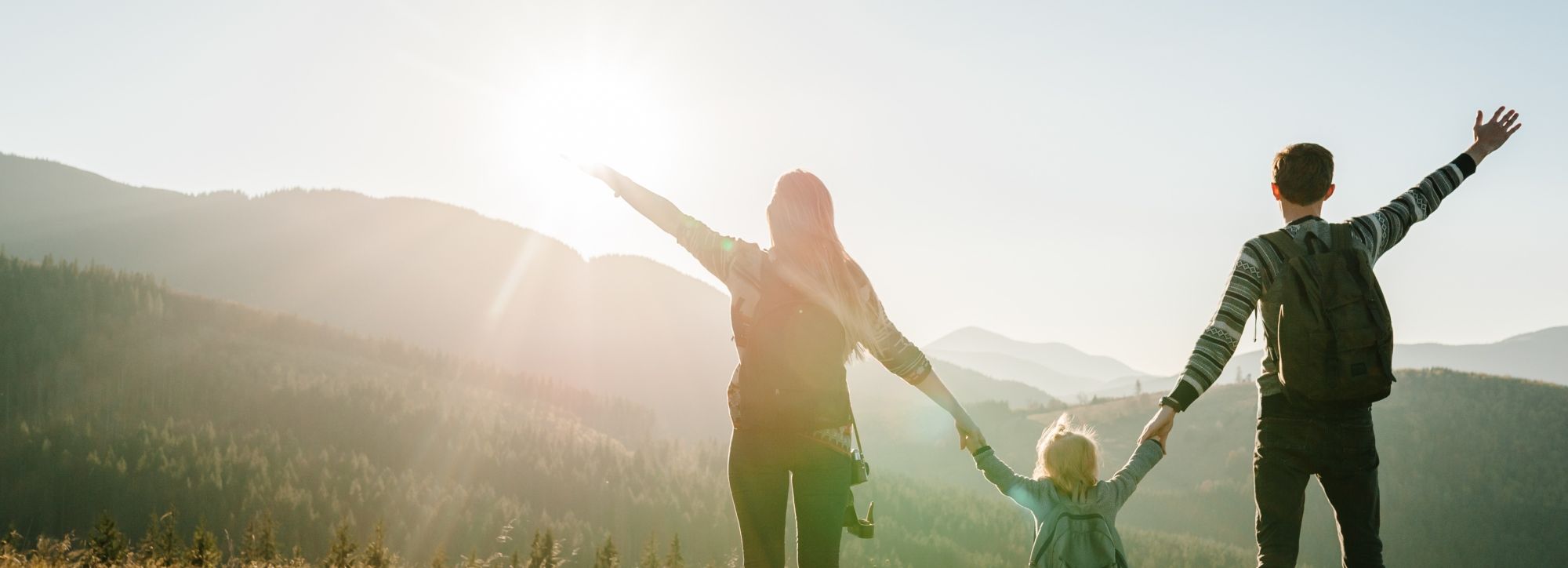 Family with backpacks enjoying a scenic view in the mountains at sunrise.