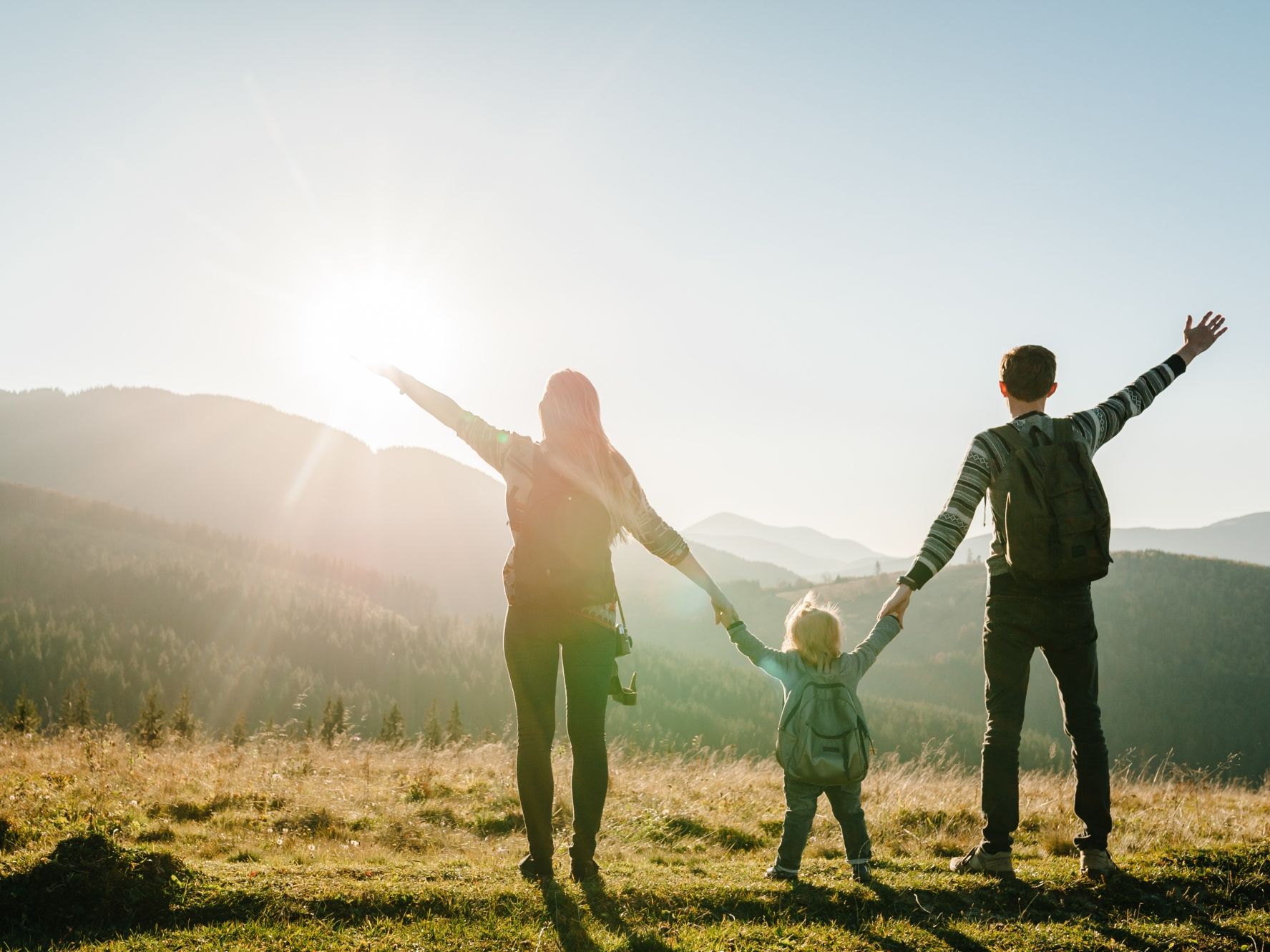 Family with backpacks enjoying a scenic view in the mountains at sunrise.