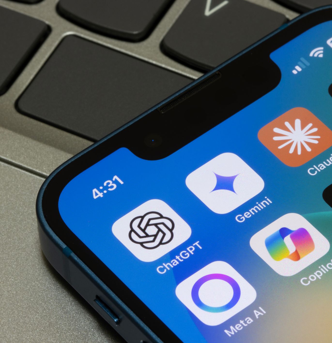 Close-up of a smartphone displaying popular AI chatbot app icons, including ChatGPT, Gemini, Claude, Perplexity, Meta AI, Copilot, and Grok, resting on a laptop keyboard.