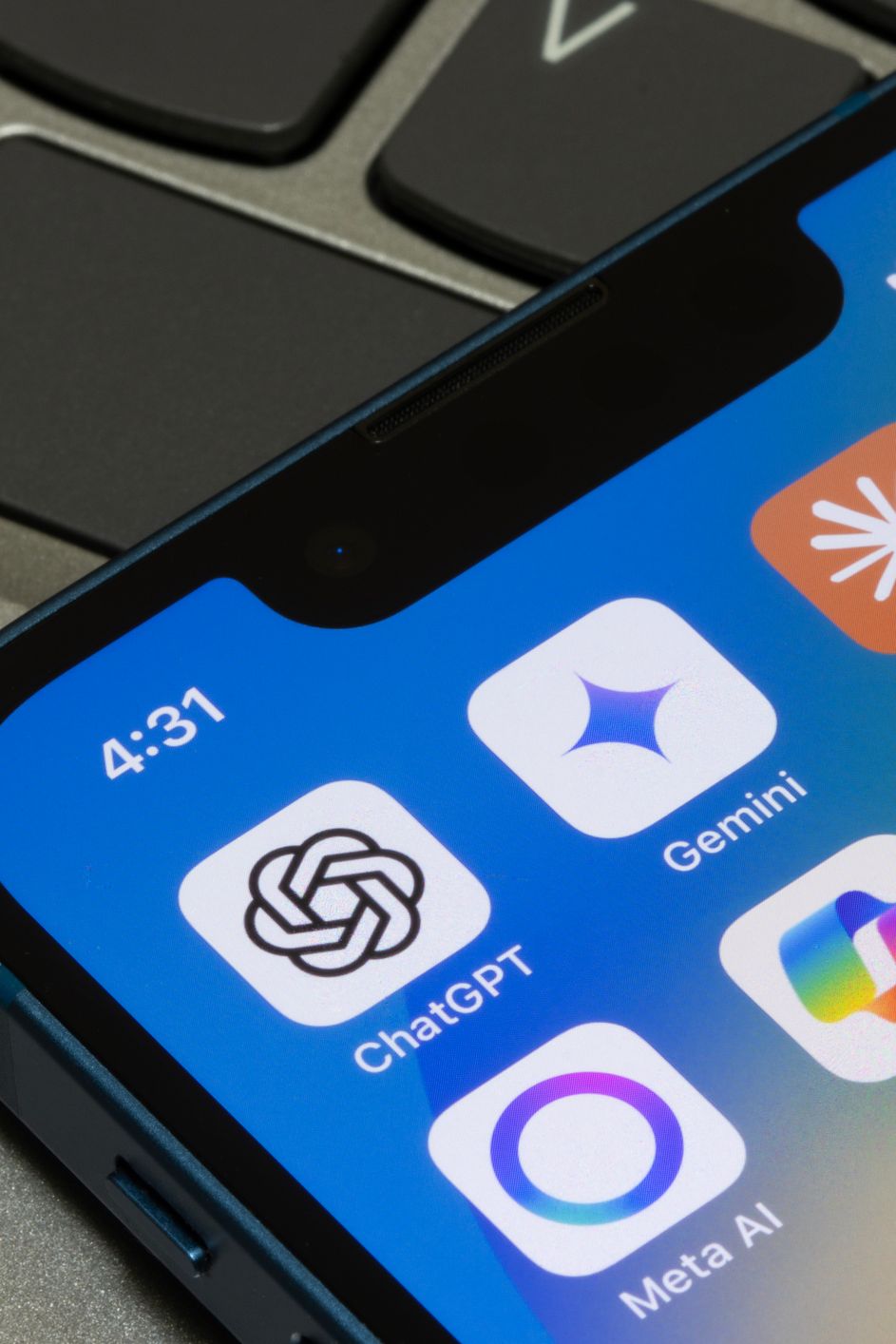 Close-up of a smartphone displaying popular AI chatbot app icons, including ChatGPT, Gemini, Claude, Perplexity, Meta AI, Copilot, and Grok, resting on a laptop keyboard.
