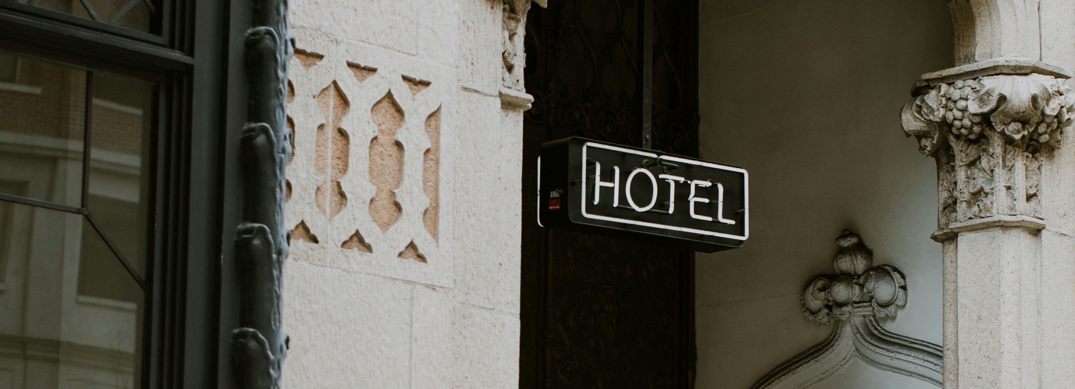 Historic hotel entrance with ornate stonework, a 'HOTEL' sign, and a luggage cart.