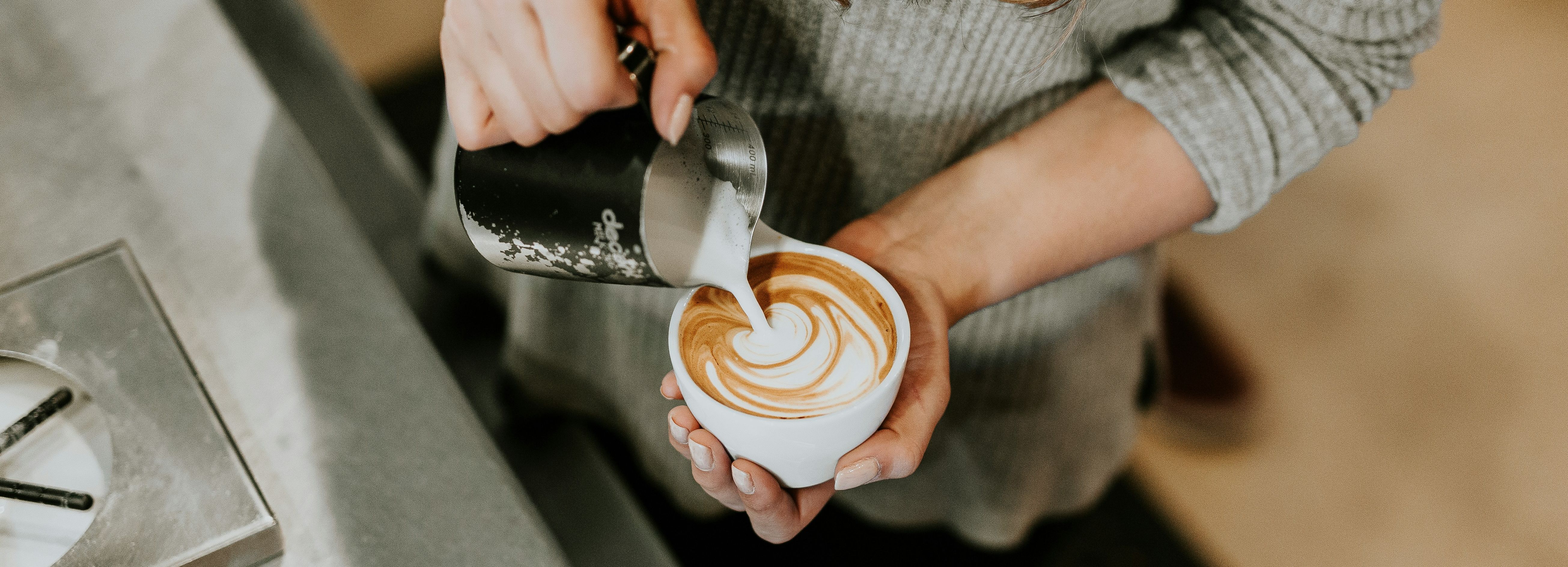 Person pouring steamed milk to create latte art in a cup of coffee