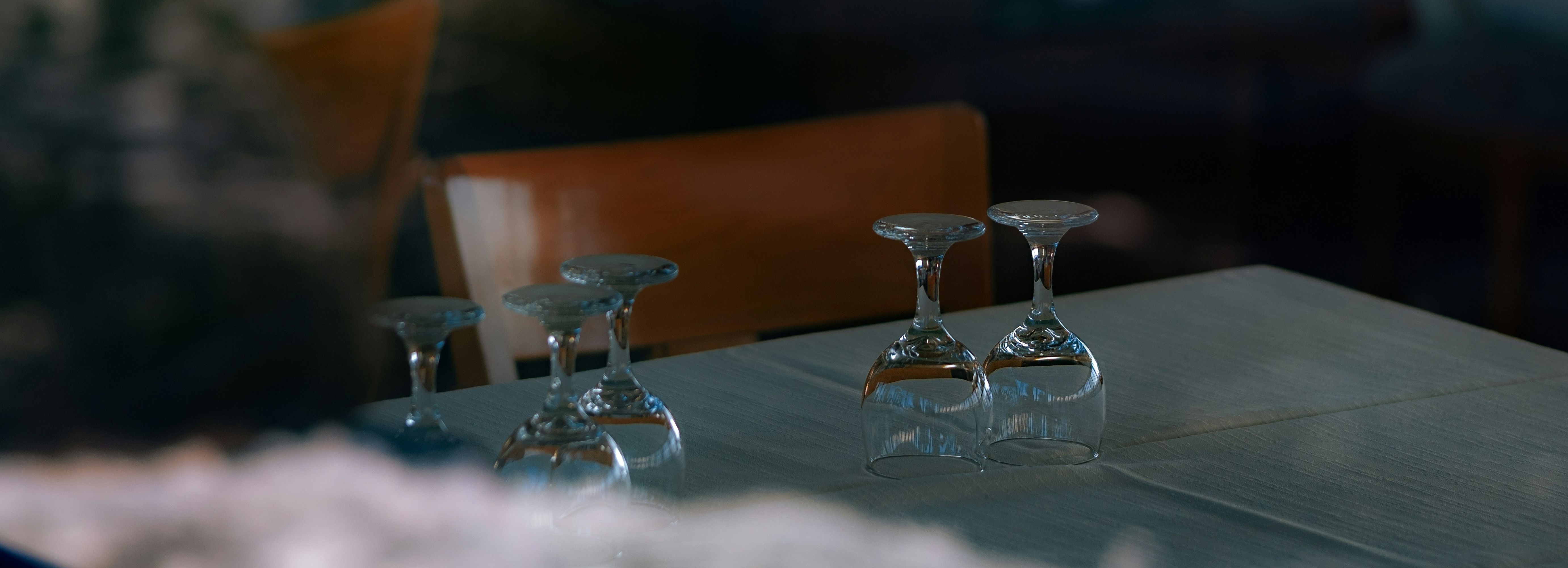 Empty restaurant table with four upside-down wine glasses placed neatly in pairs, and wooden chairs in the background.