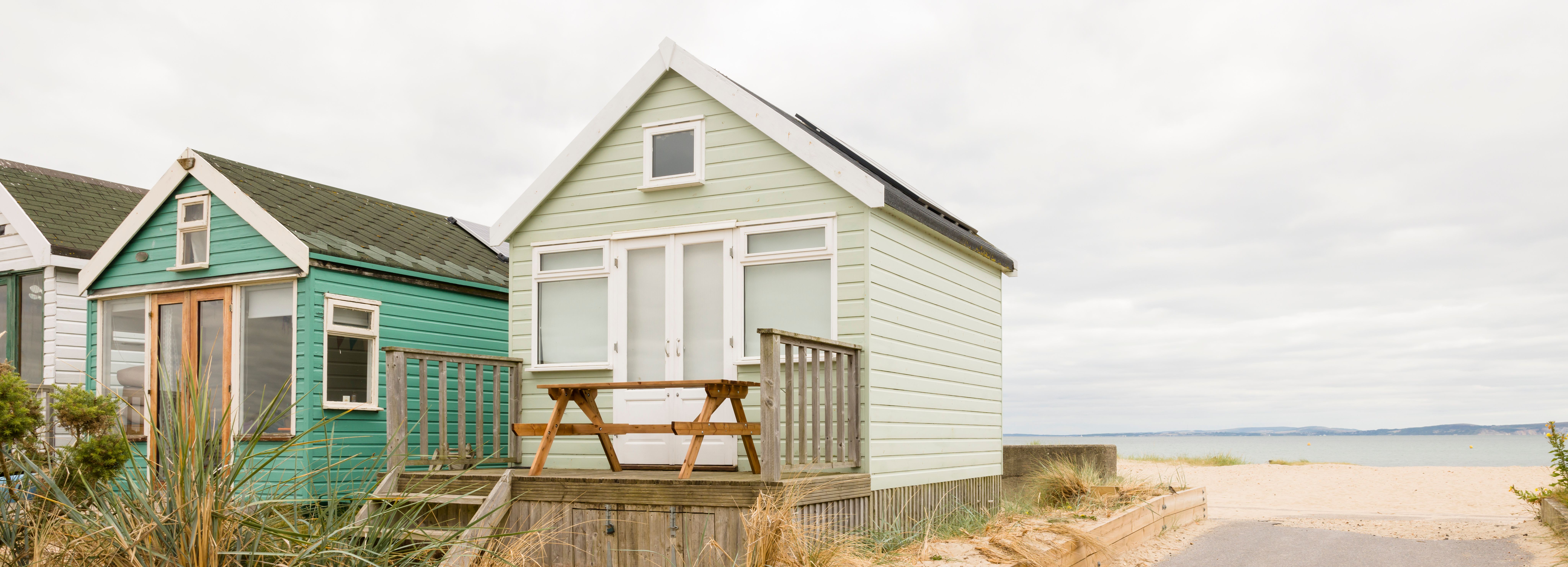 Beach huts on a sandy coastline with a picnic table on the deck and a pathway leading to the sea