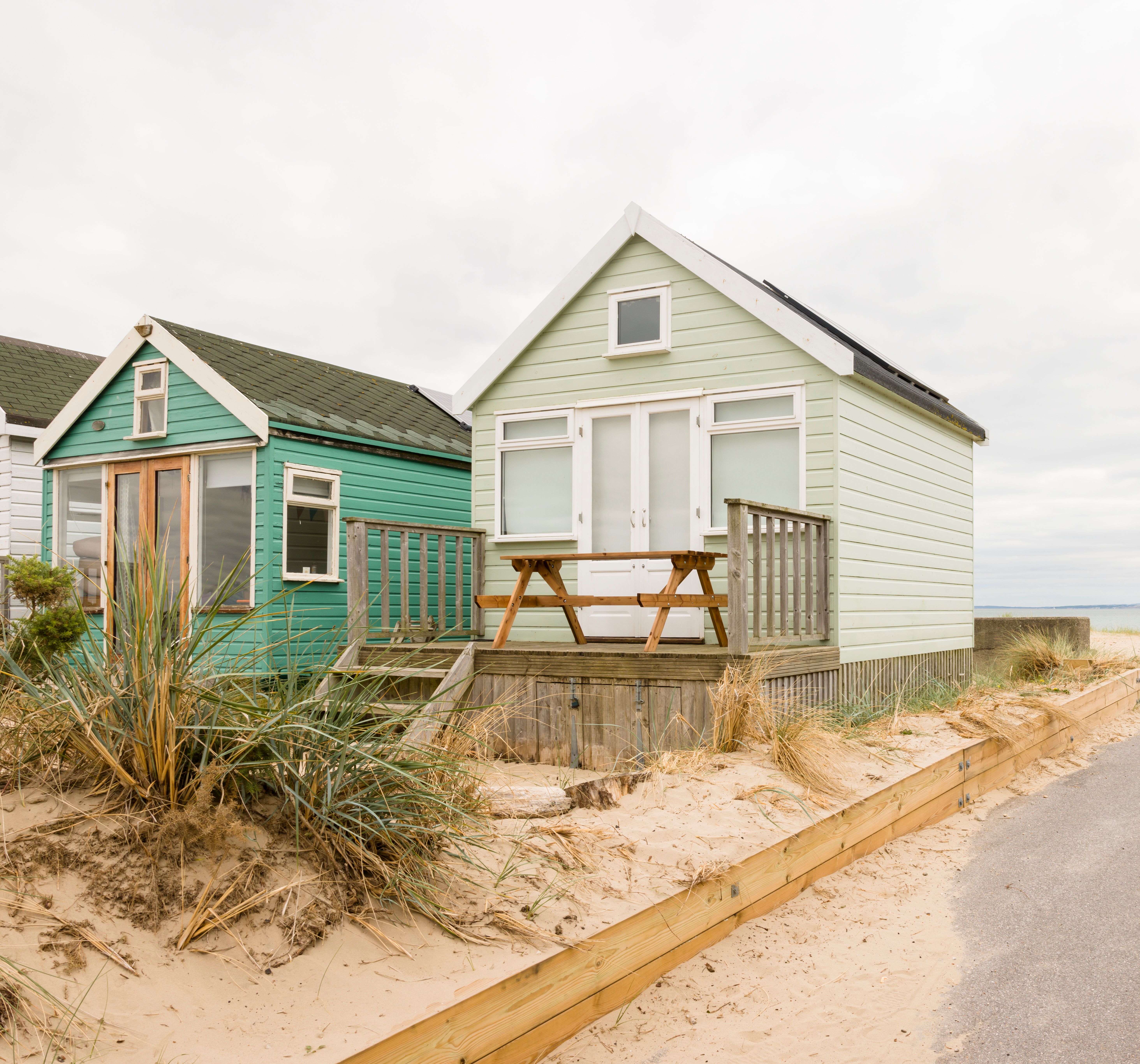 Beach huts on a sandy coastline with a picnic table on the deck and a pathway leading to the sea