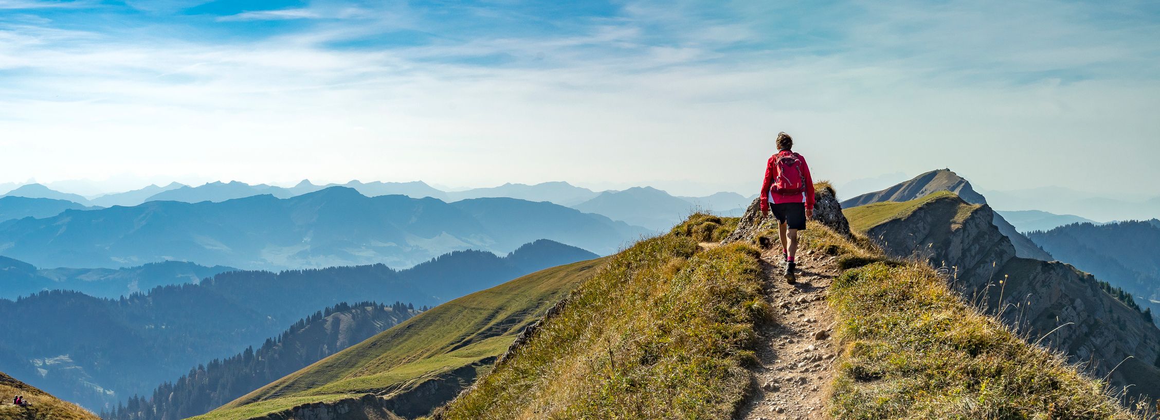 Person hiking on a mountain ridge with a scenic mountain range in the background