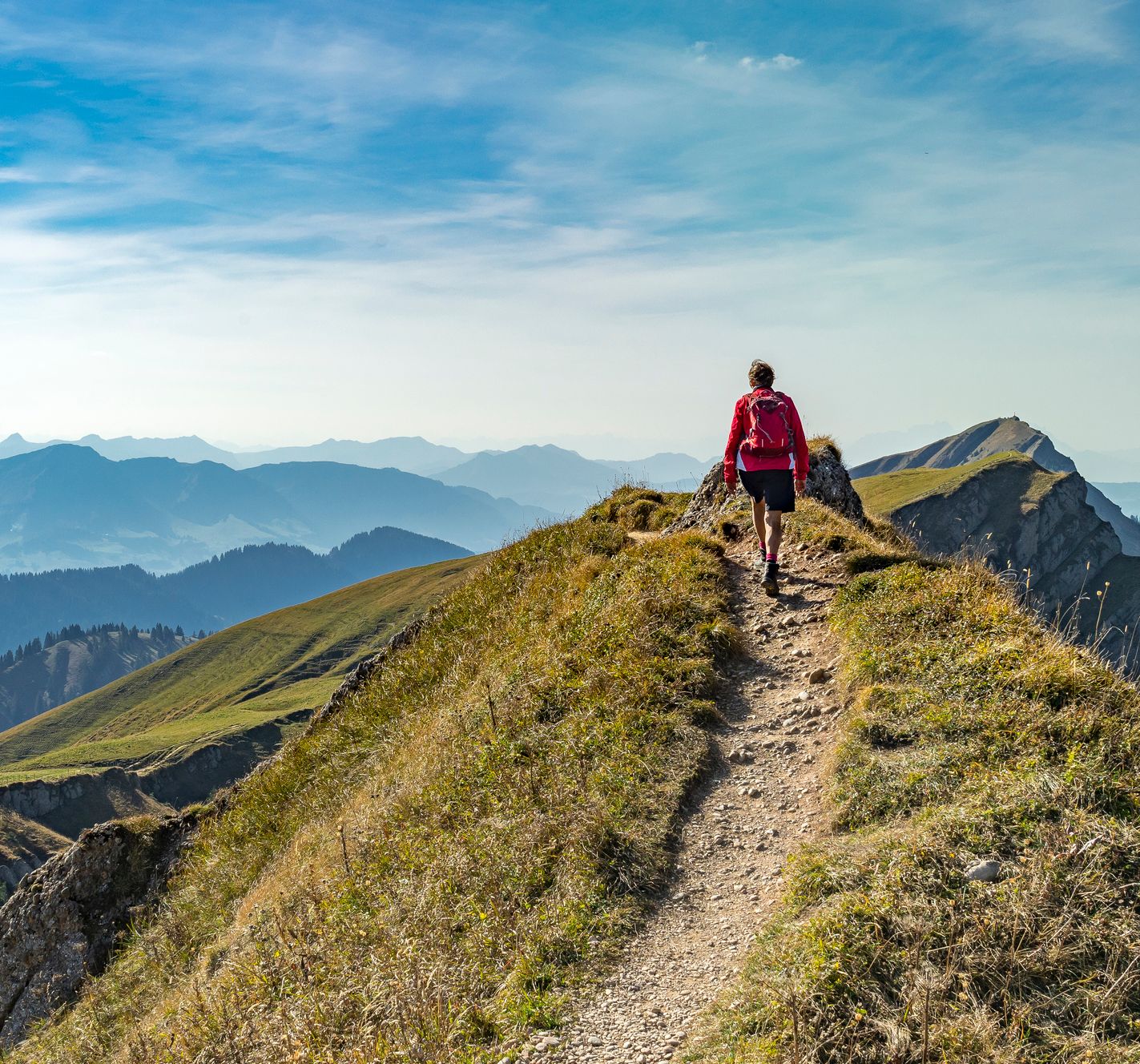 Person hiking on a mountain ridge with a scenic mountain range in the background