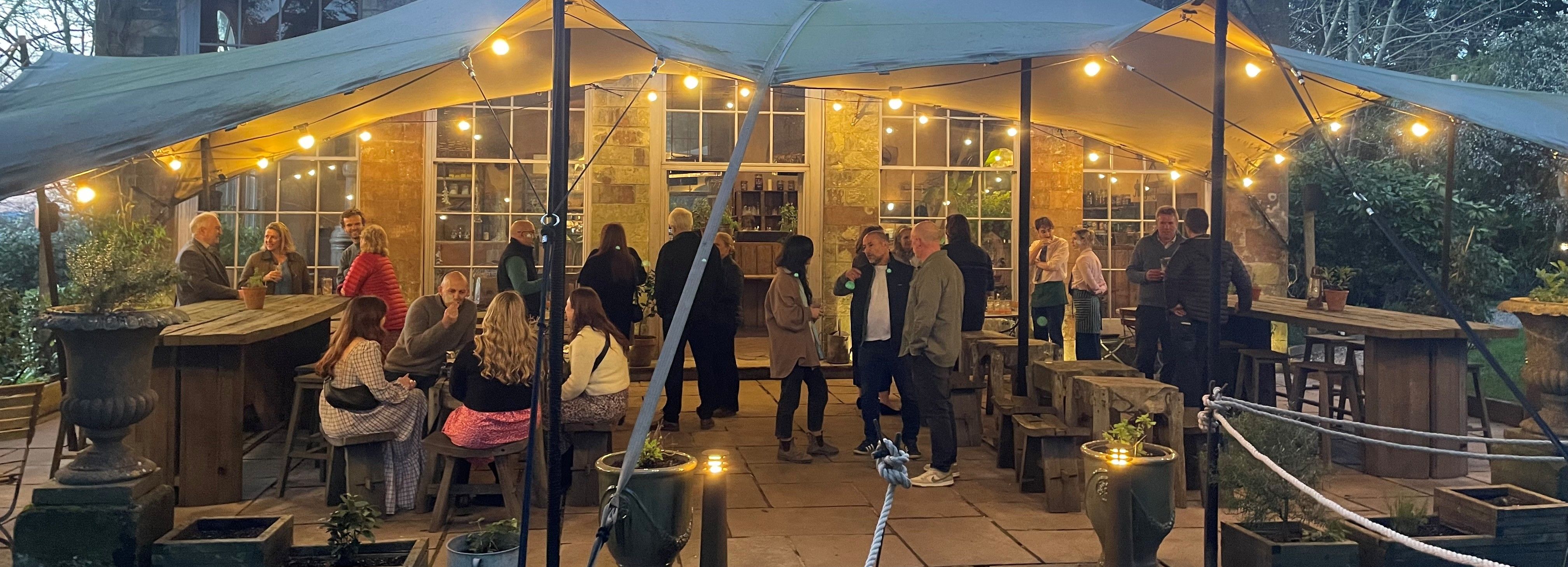 Outdoor gathering under a canopy with string lights in front of a stone building