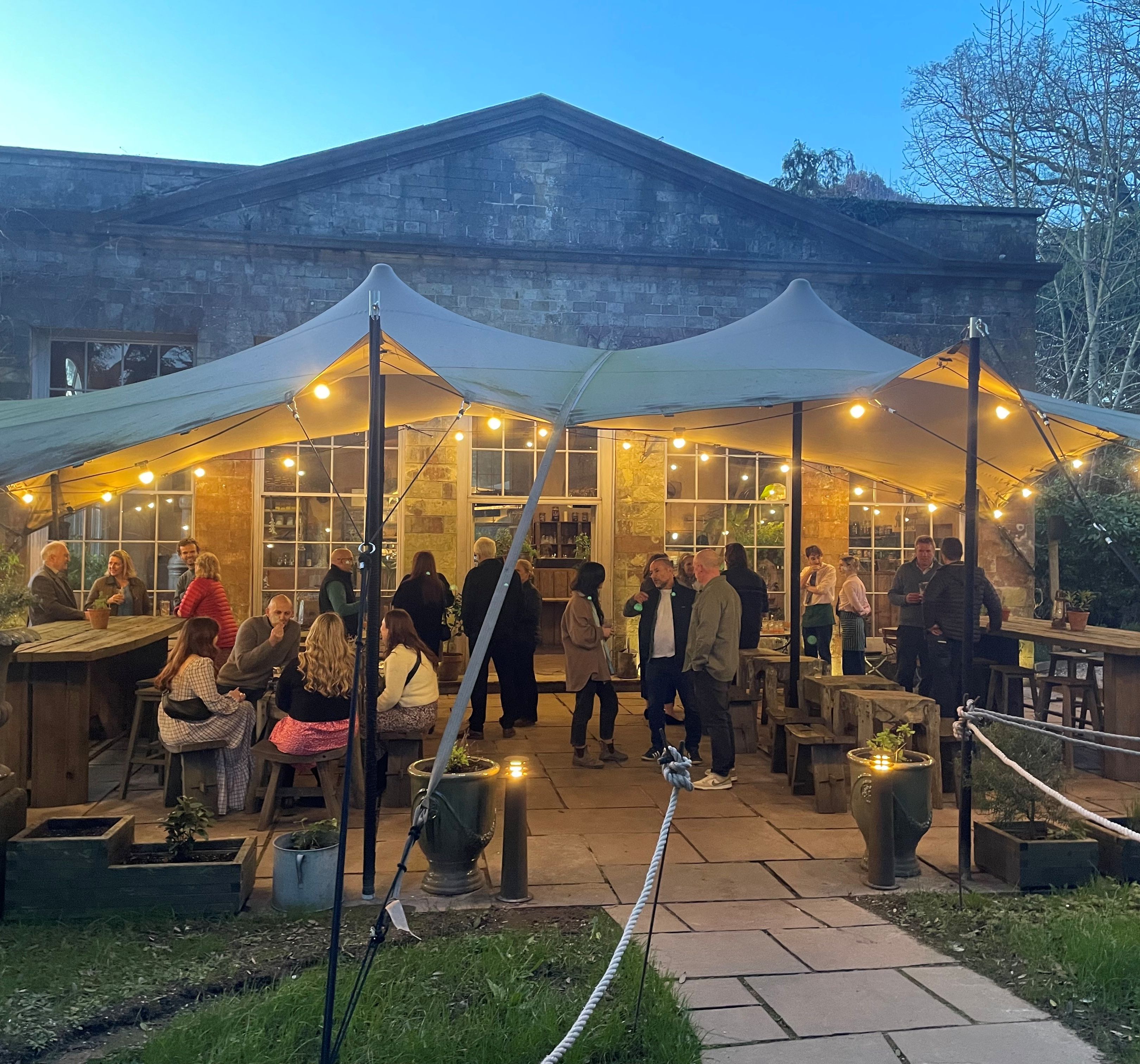 Outdoor gathering under a canopy with string lights in front of a stone building
