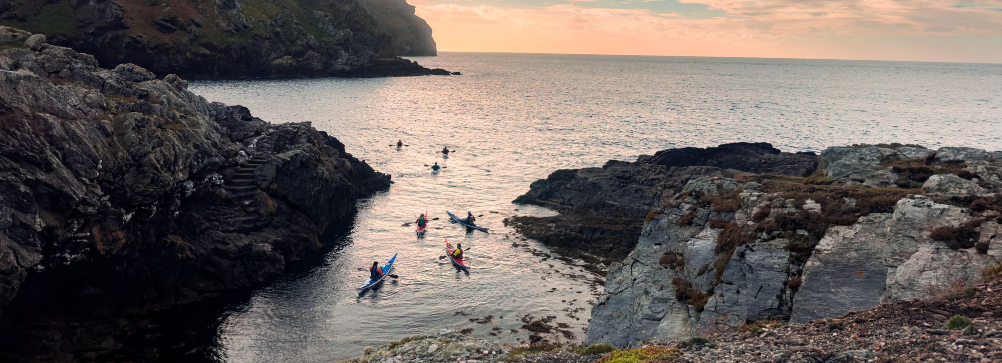 Group of kayakers paddling through a rocky coastal cove at sunset