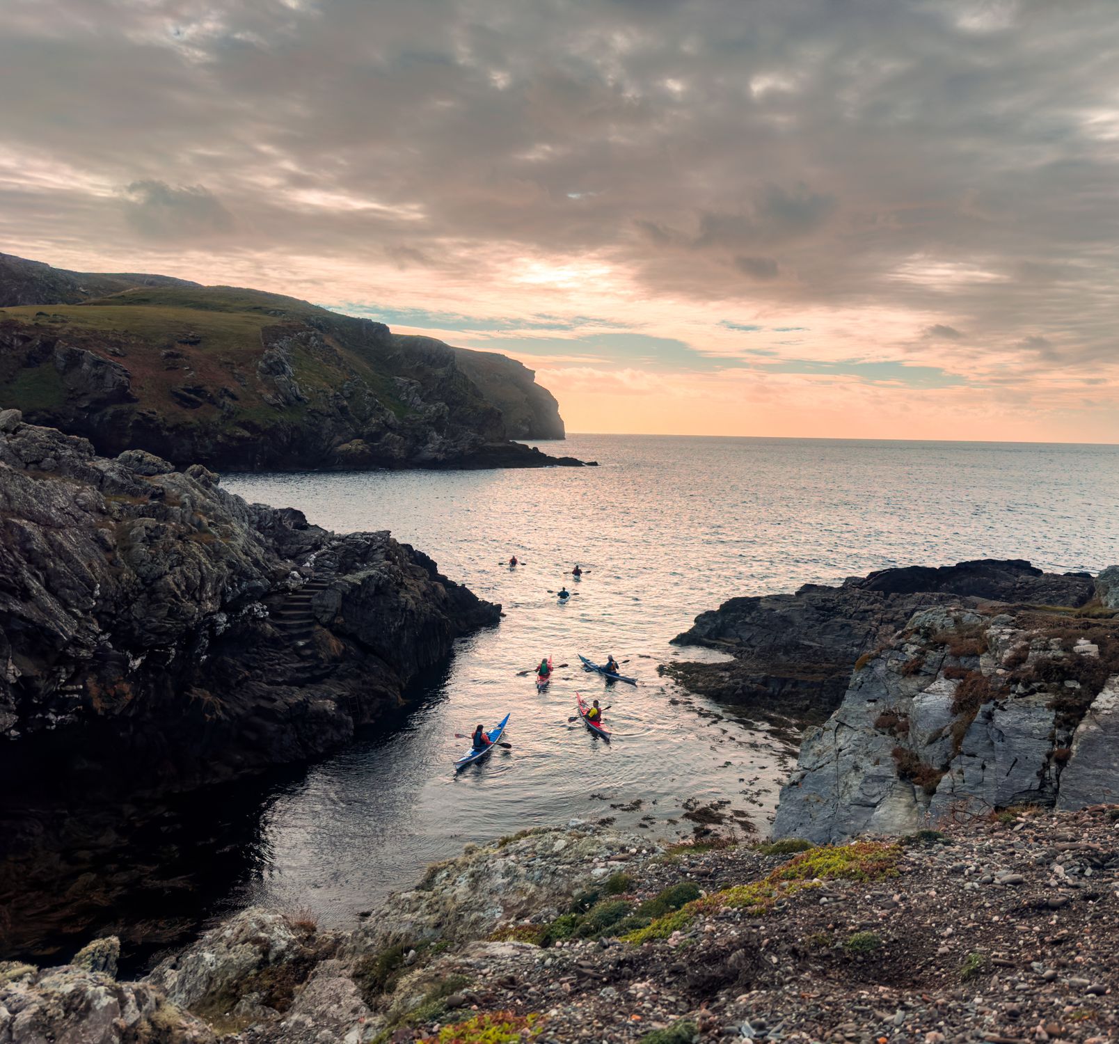 Group of kayakers paddling through a rocky coastal cove at sunset