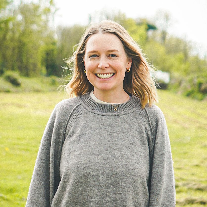 Woman smiling outdoors in a green field, wearing a grey sweater