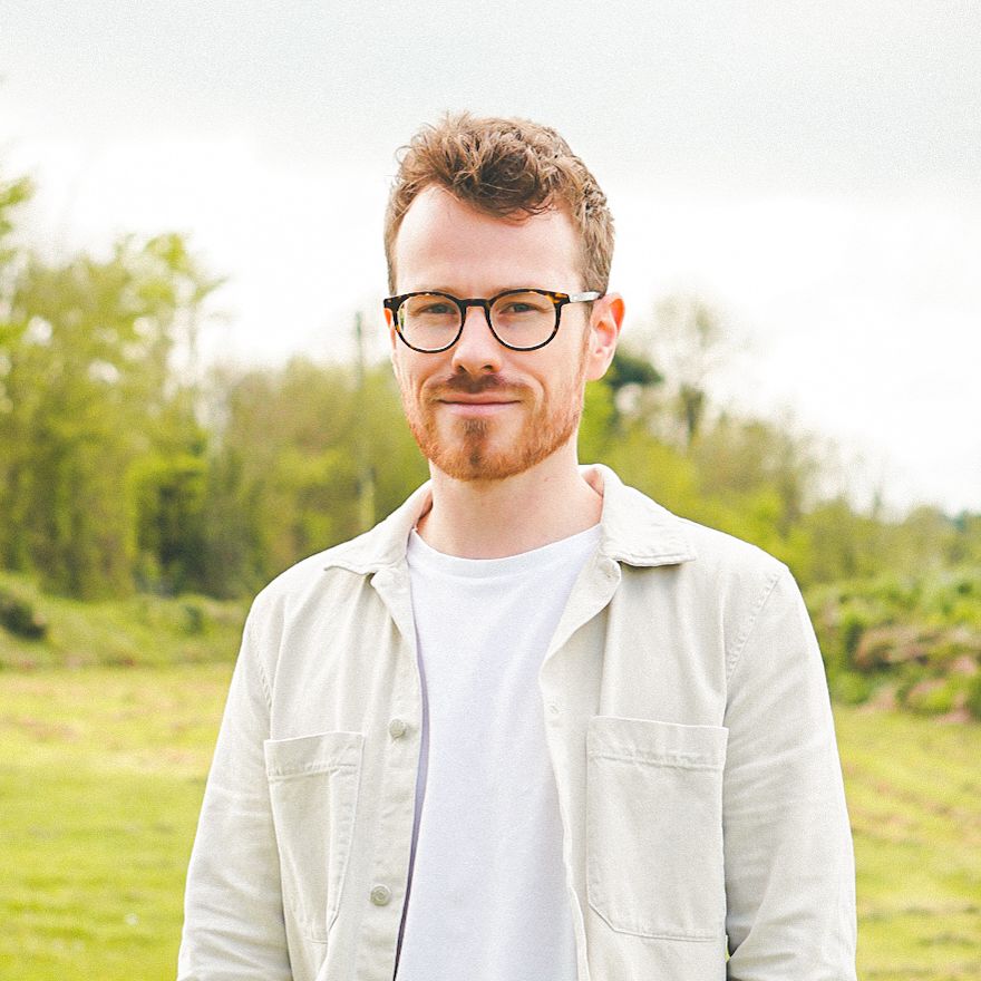 Man with glasses and beard standing outdoors in a grassy field