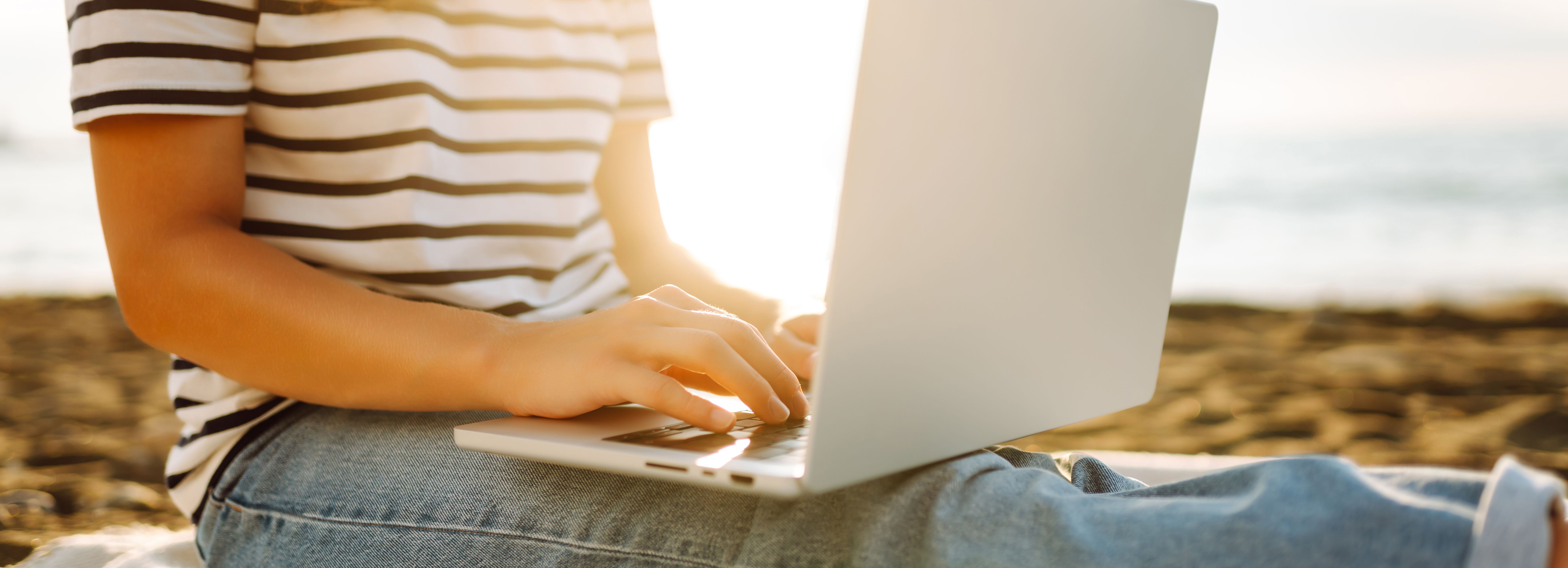 Person sitting on beach using a laptop