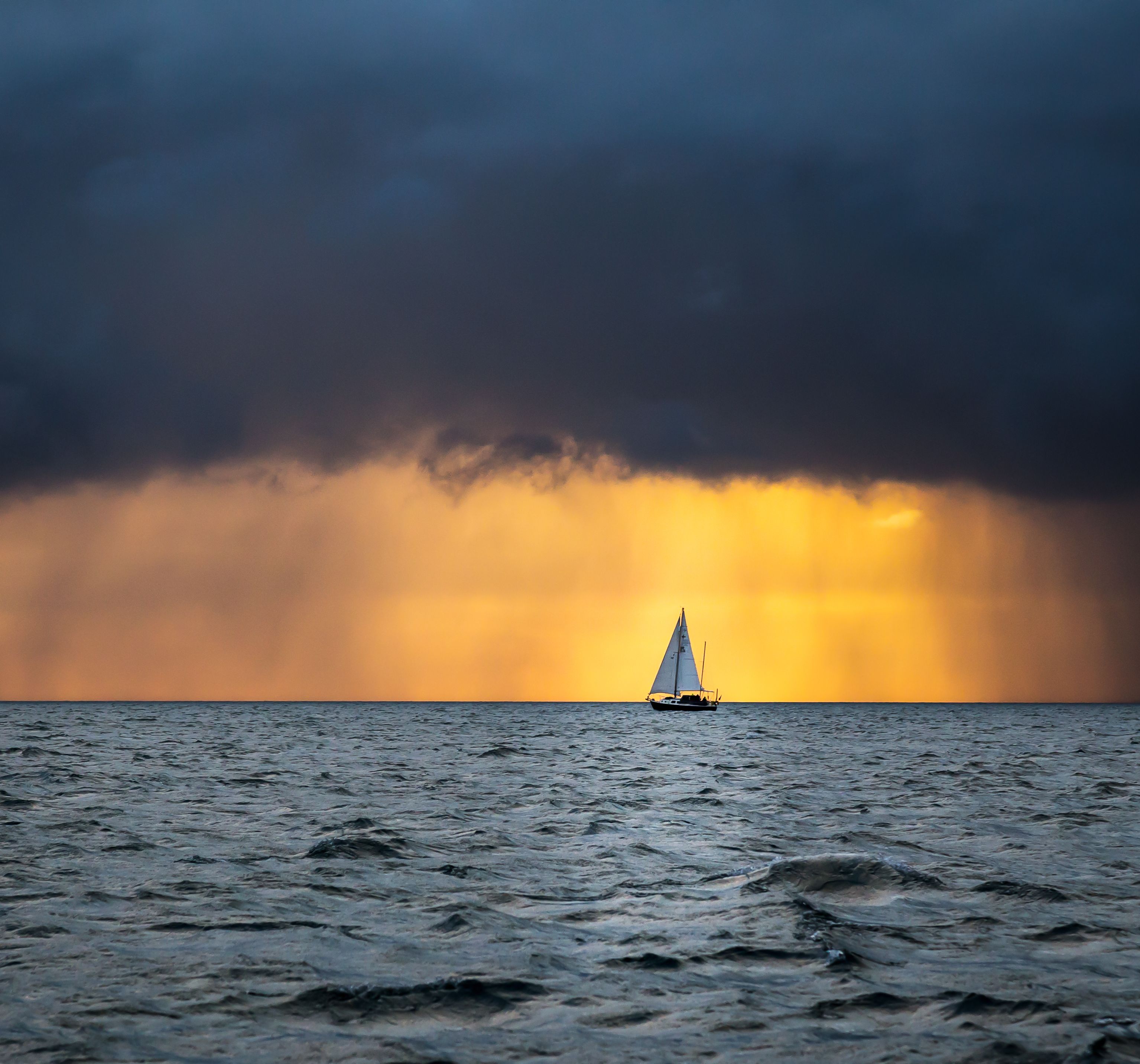 Sailboat on the ocean with dramatic clouds and golden sunset in the background