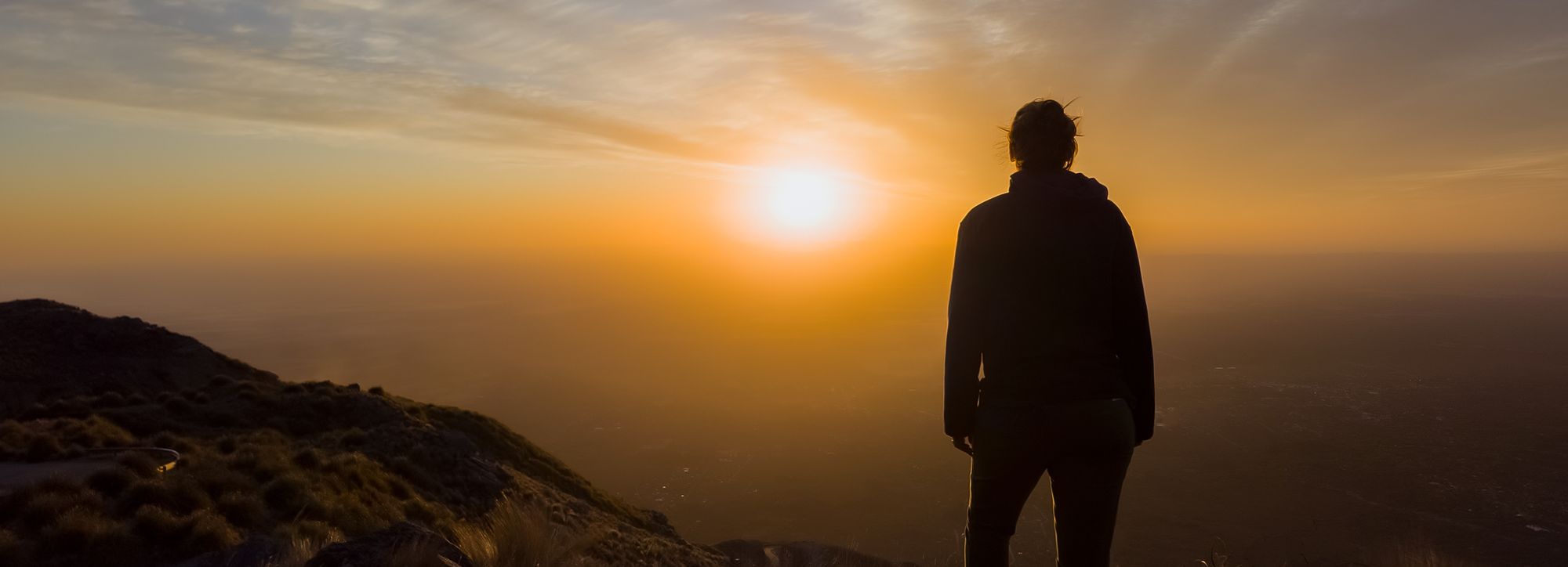 Silhouette of a person standing on a mountain top overlooking a sunset