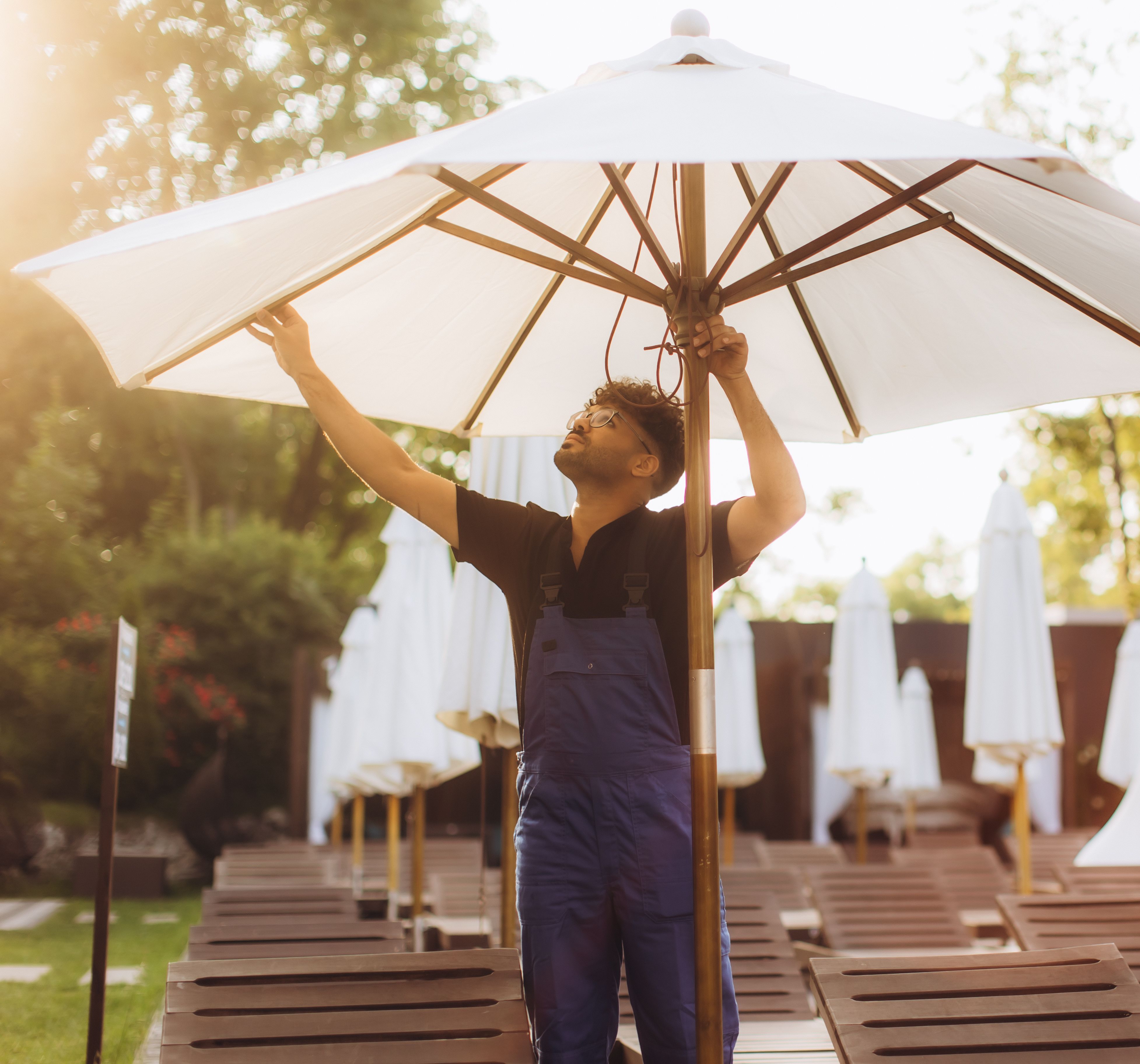 Man adjusting a large outdoor umbrella by the poolside