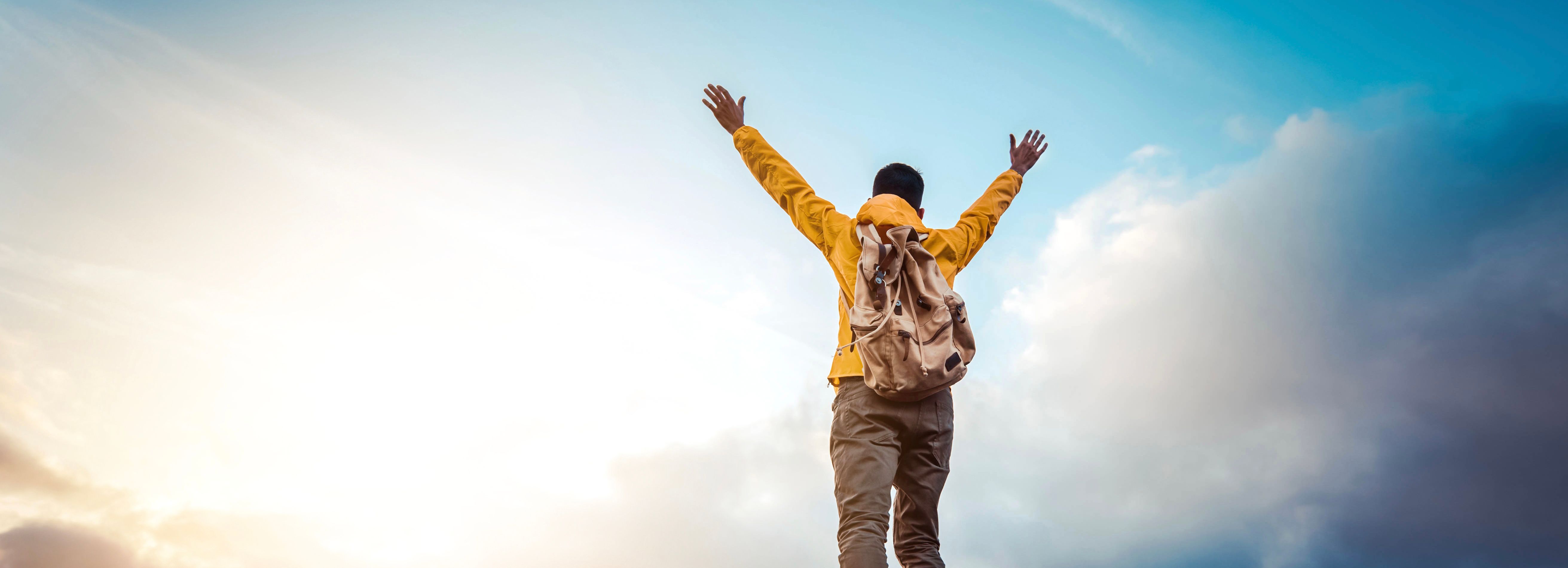 Person standing on top of a mountain with arms raised in victory at sunrise or sunset