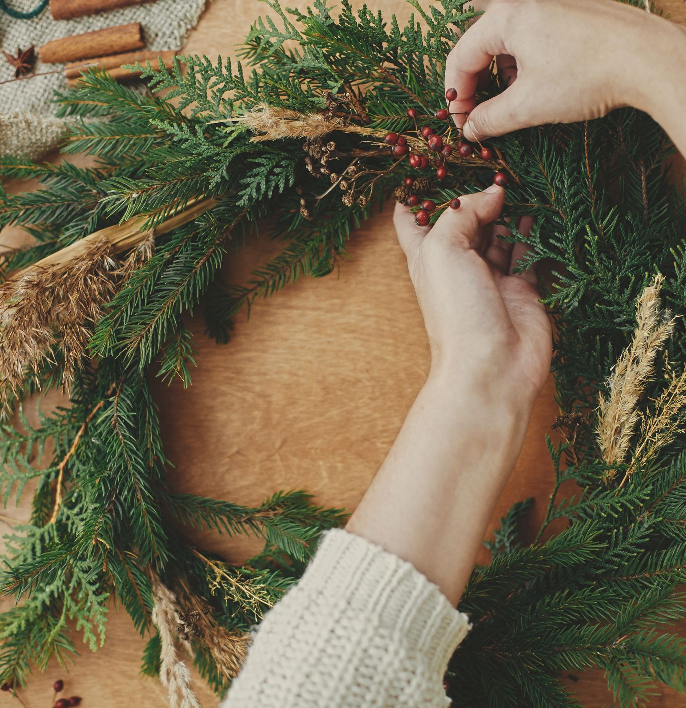 Hands decorating a homemade Christmas wreath with red berries and dried plants