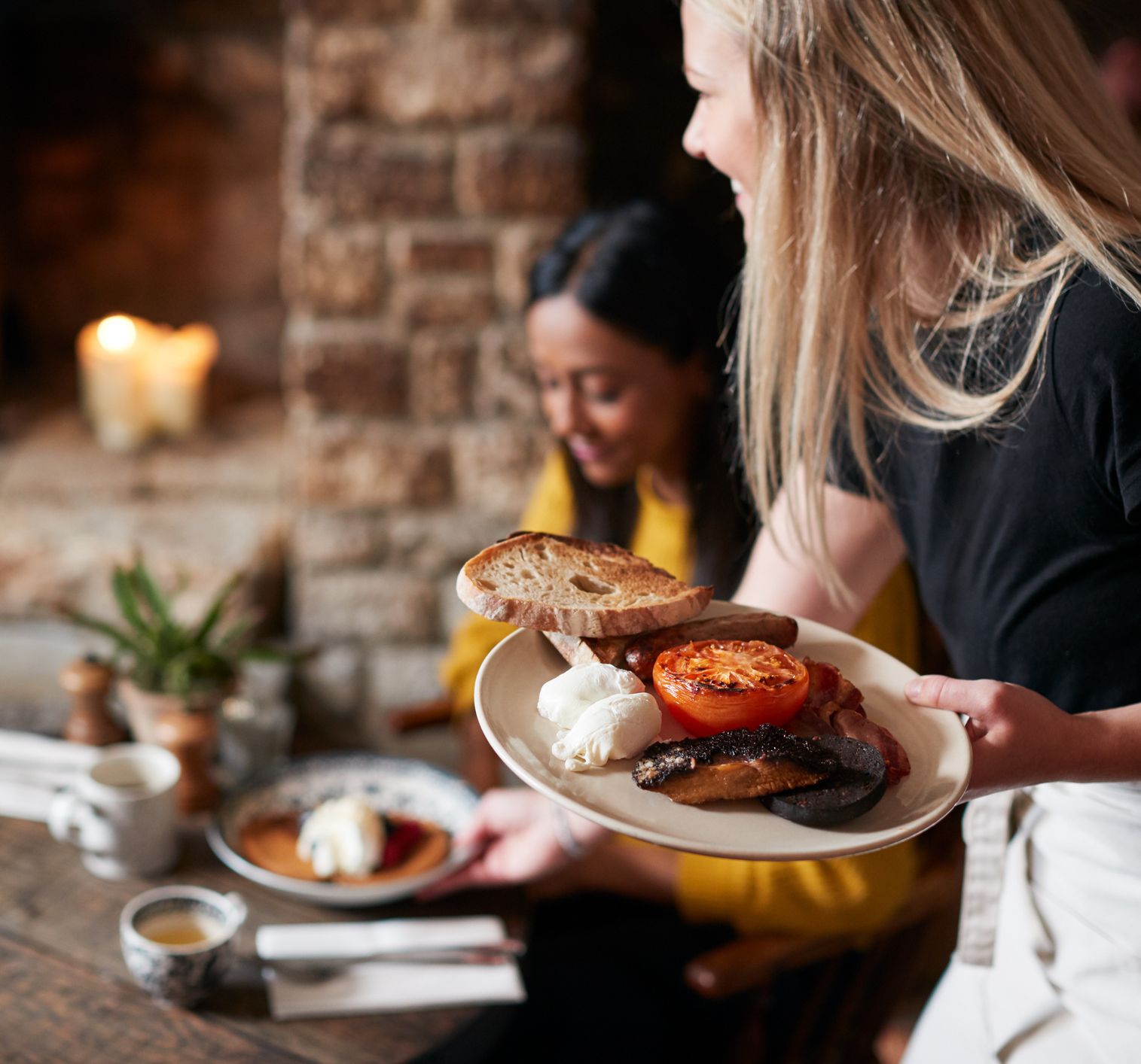 Waitress serving a plate of traditional English breakfast to a customer at a cozy restaurant