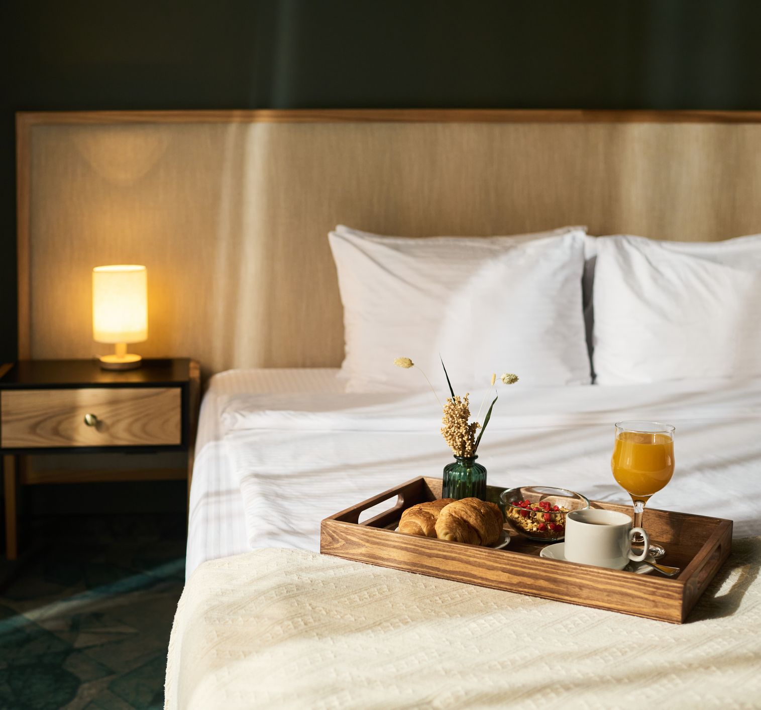 Breakfast tray with croissants, coffee, orange juice, and flowers on bed in cozy hotel room