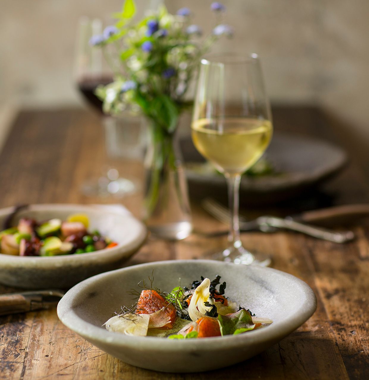Dinner and wine on table with bunch of wildflowers