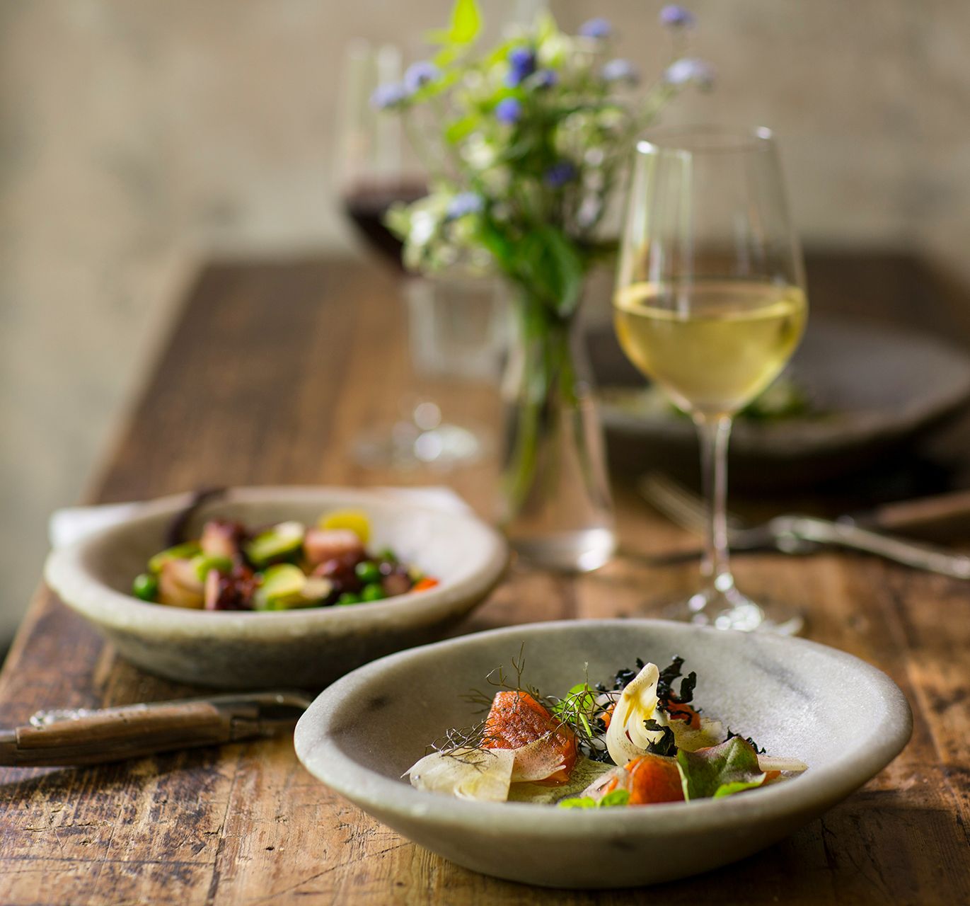 Dinner and wine on table with bunch of wildflowers