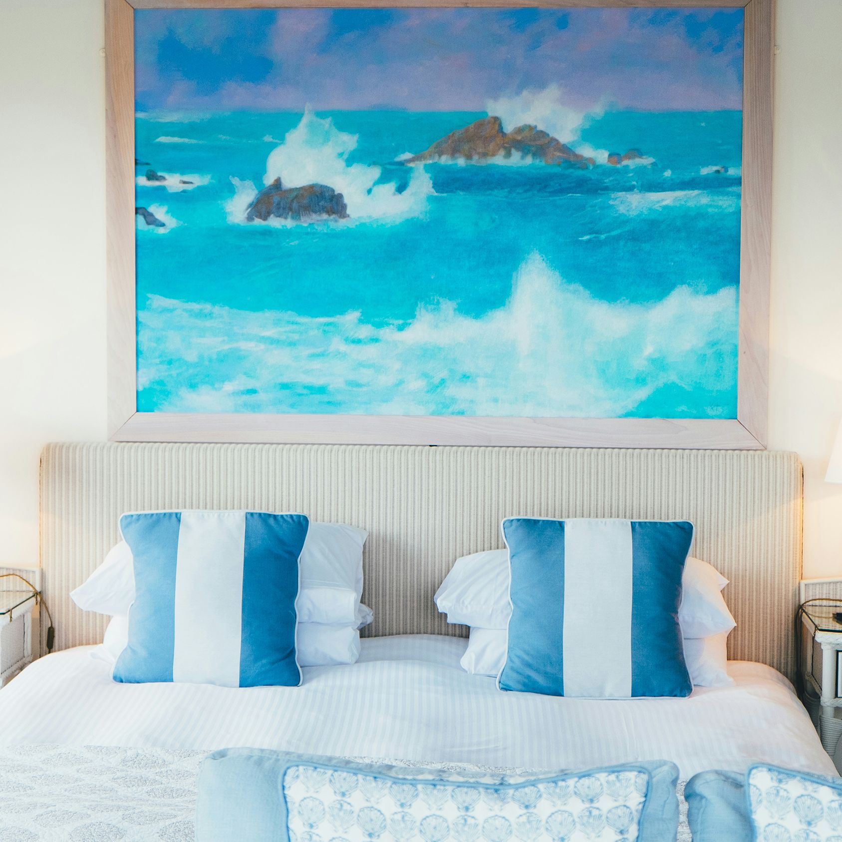 Bed with blue stripe cushions and coastal painting