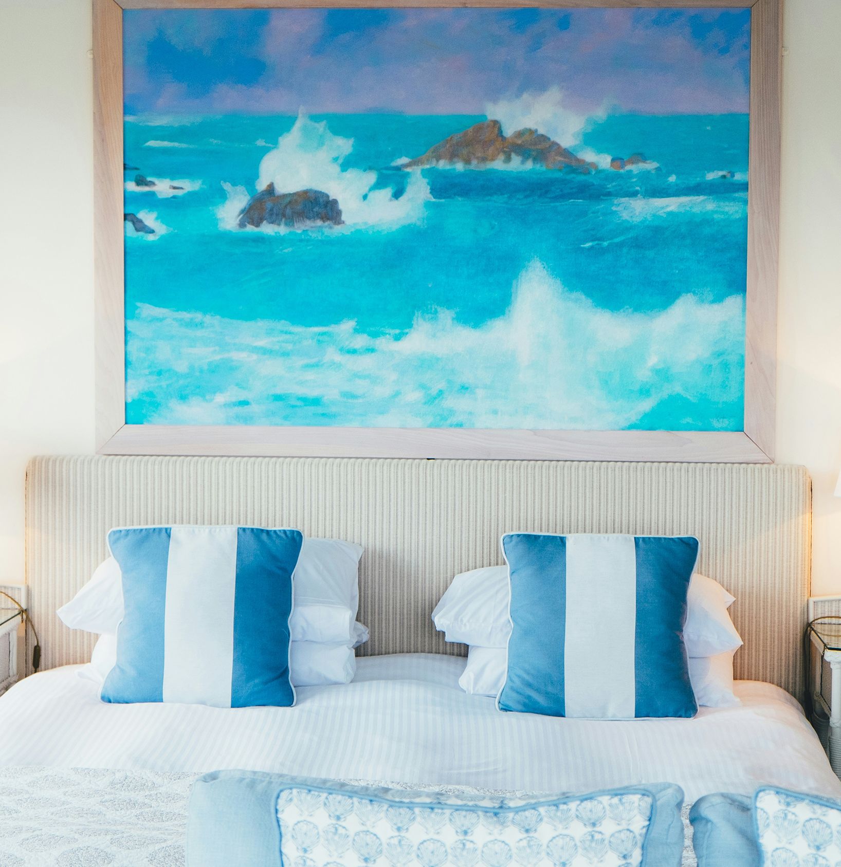Bed with blue stripe cushions and coastal painting