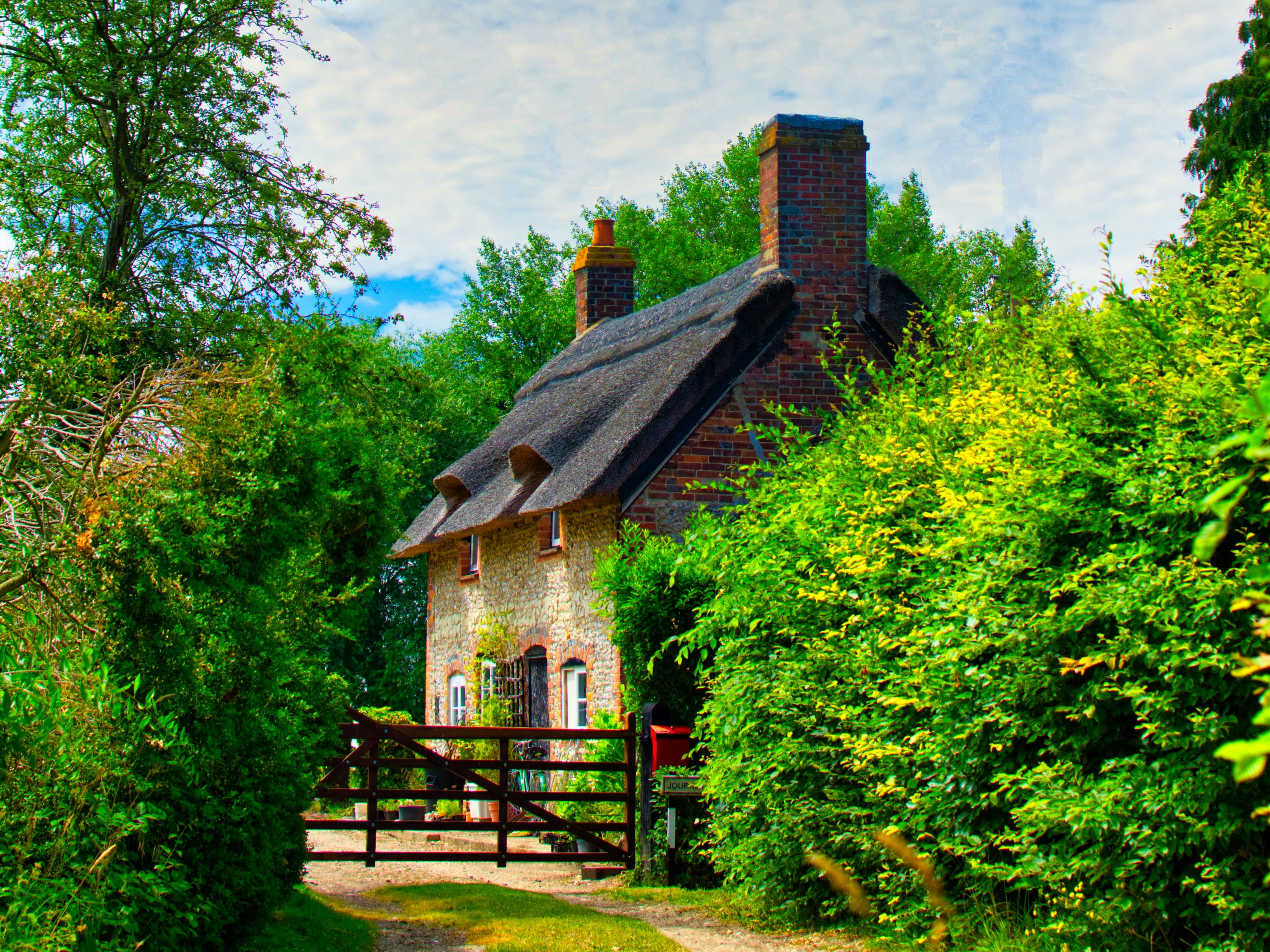 Quaint stone cottage with a thatched roof surrounded by lush greenery and trees