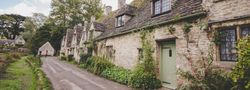 Row of charming stone cottages with mossy roofs and climbing plants in a countryside village.