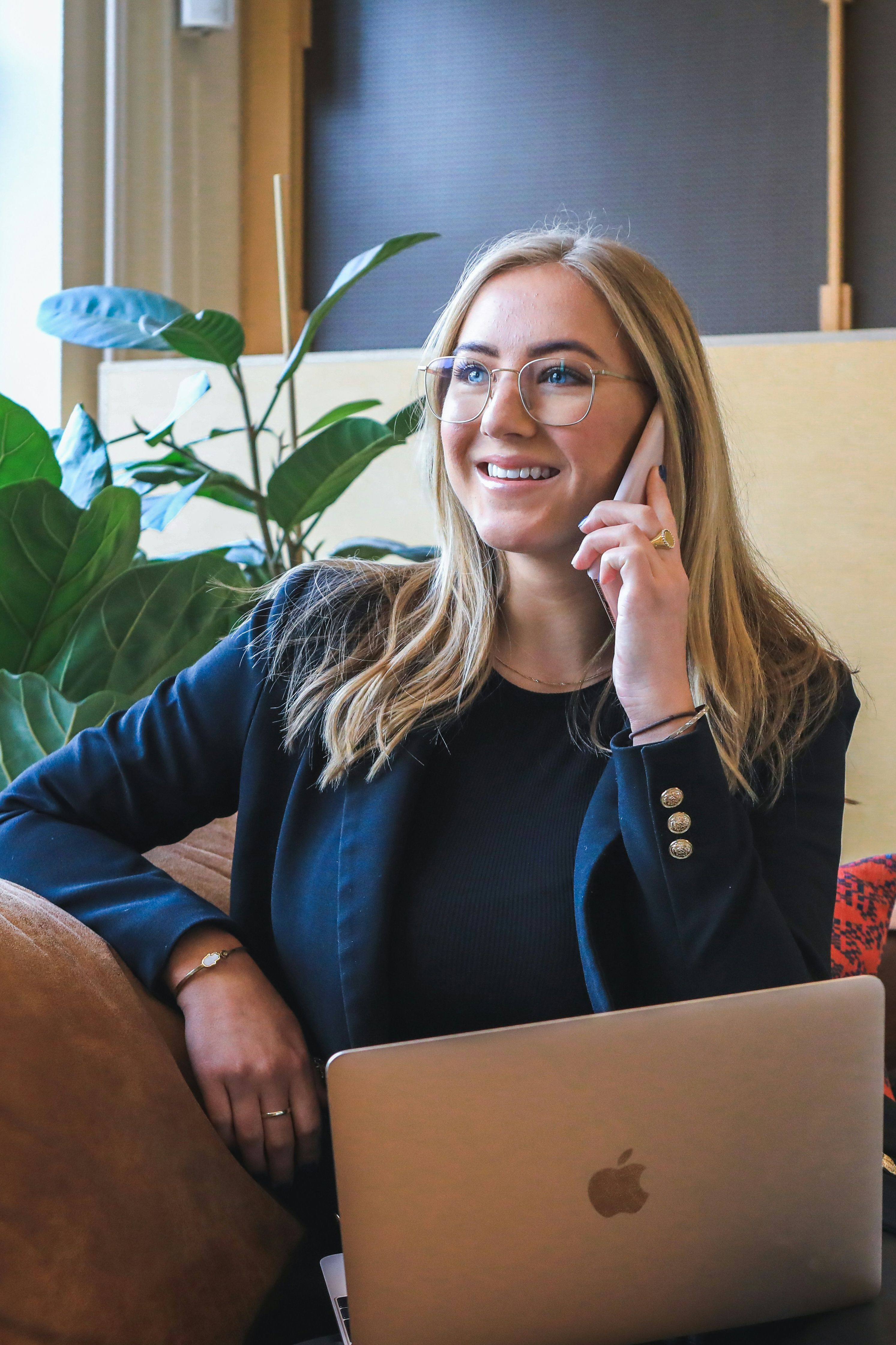 Woman sitting on a sofa with a laptop, smiling and talking on the phone in a modern office setting