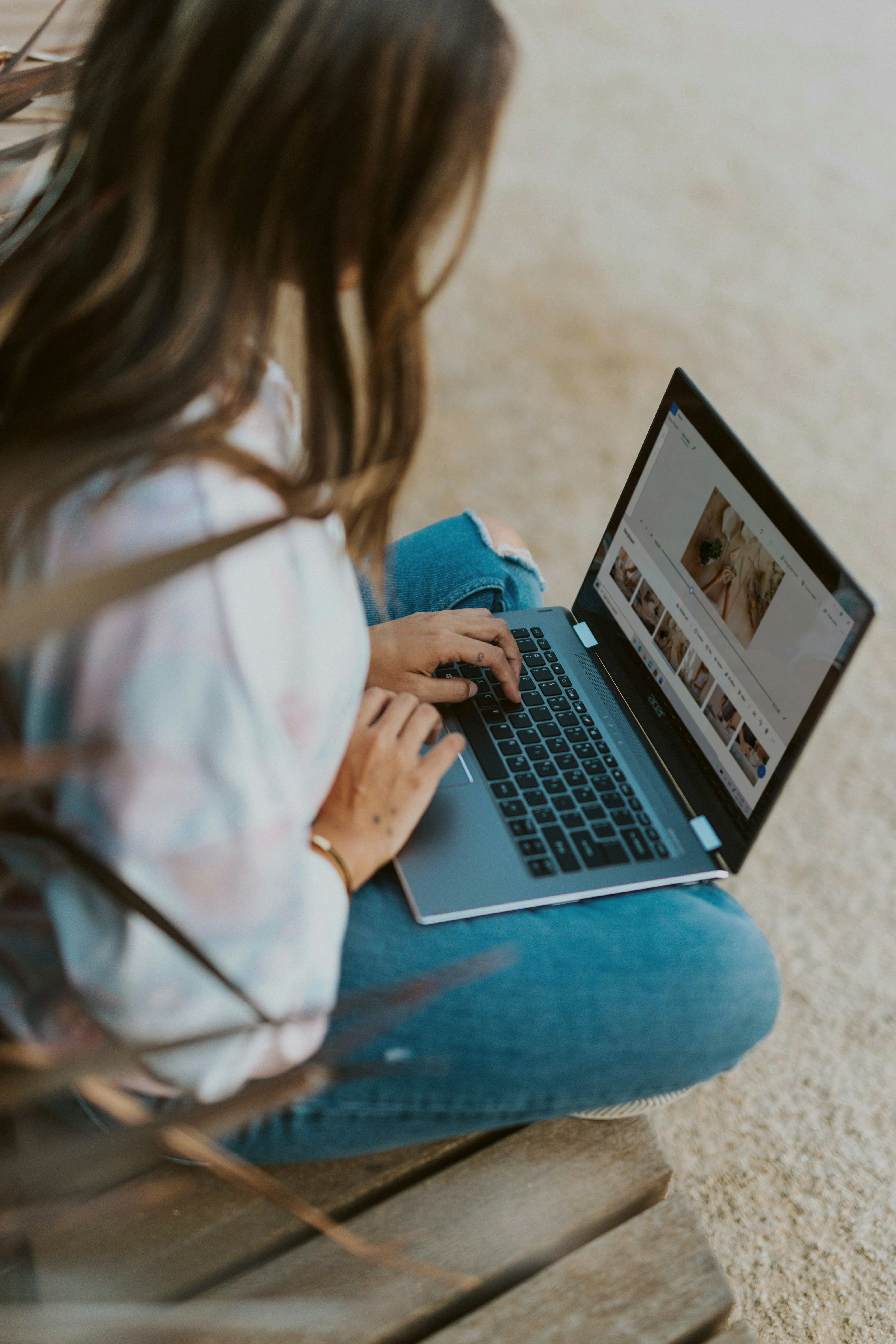 Person using a laptop while sitting outdoors on a wooden bench.