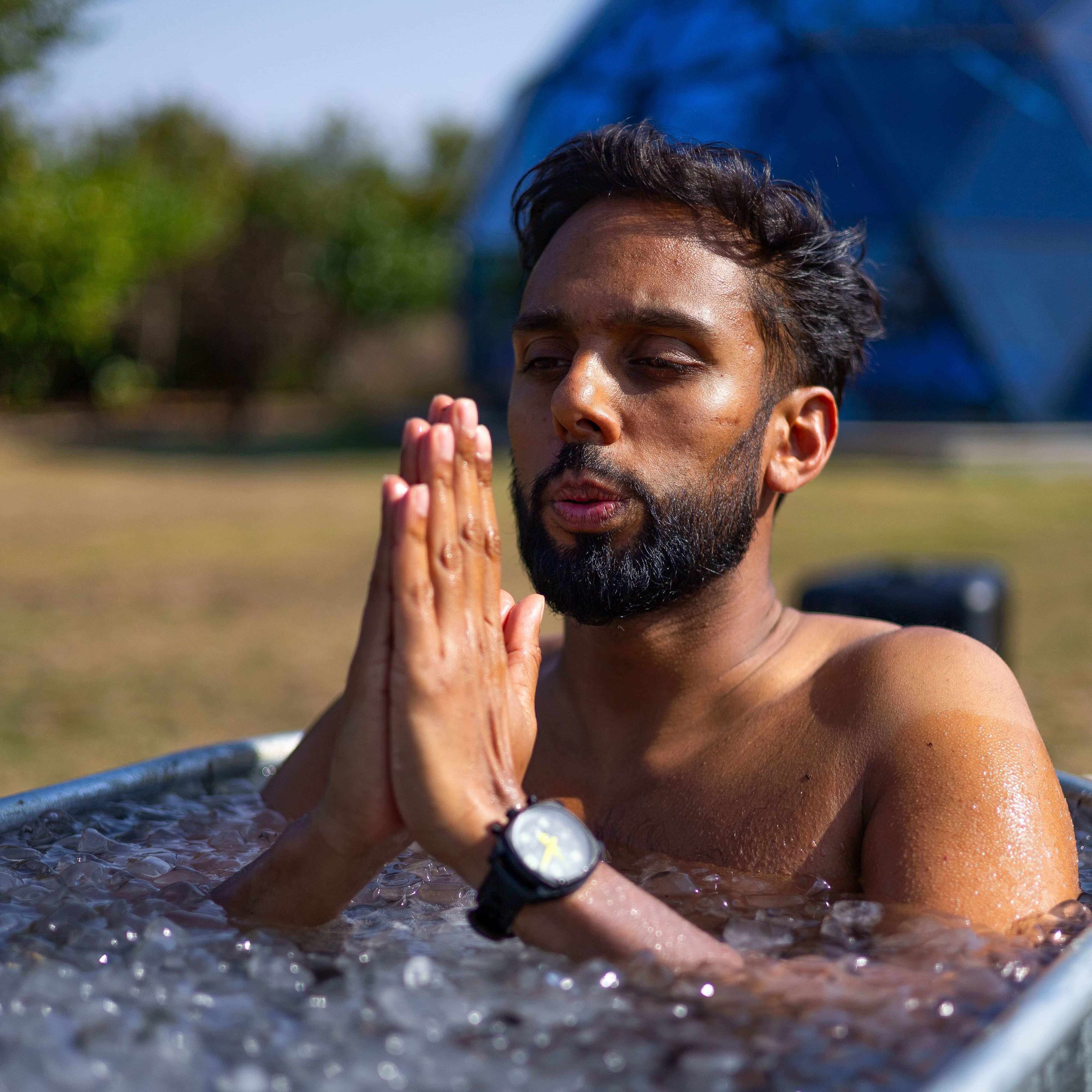 Man meditating in an ice bath outdoors with hands in prayer position
