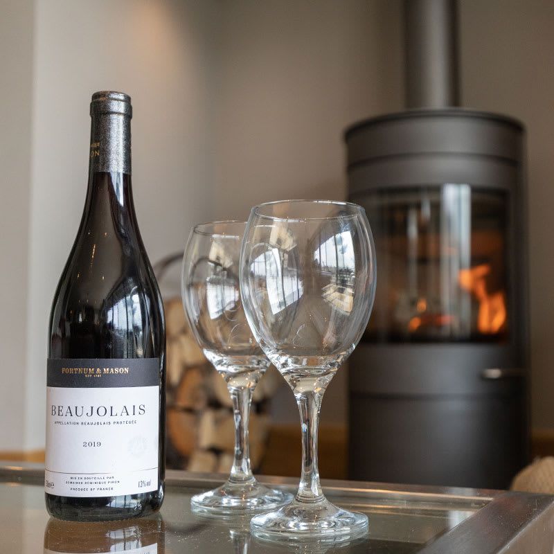 Bottle of Beaujolais wine with two empty wine glasses in front of a fireplace