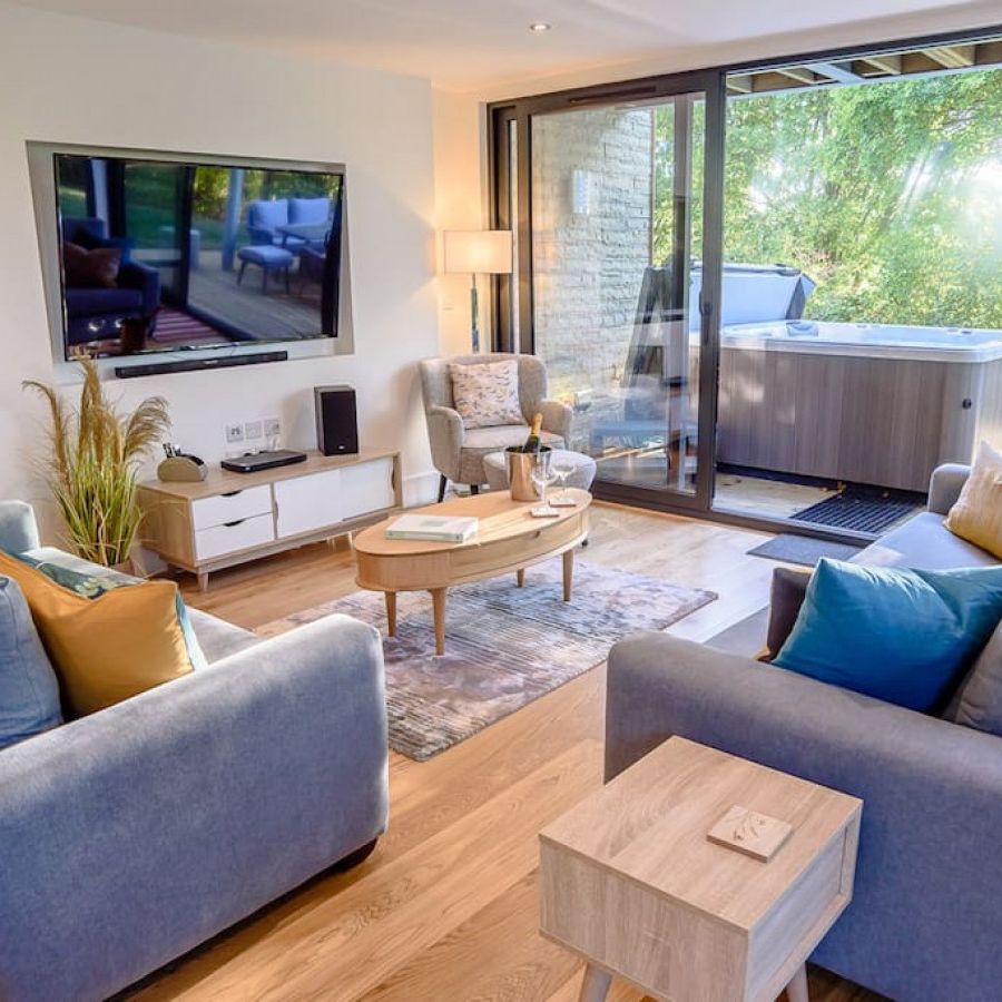 Modern living room with large windows, cozy sofas, and a view of a hot tub outside