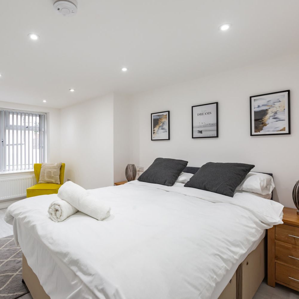 Modern bedroom with white walls, bed, yellow chair, and framed artwork