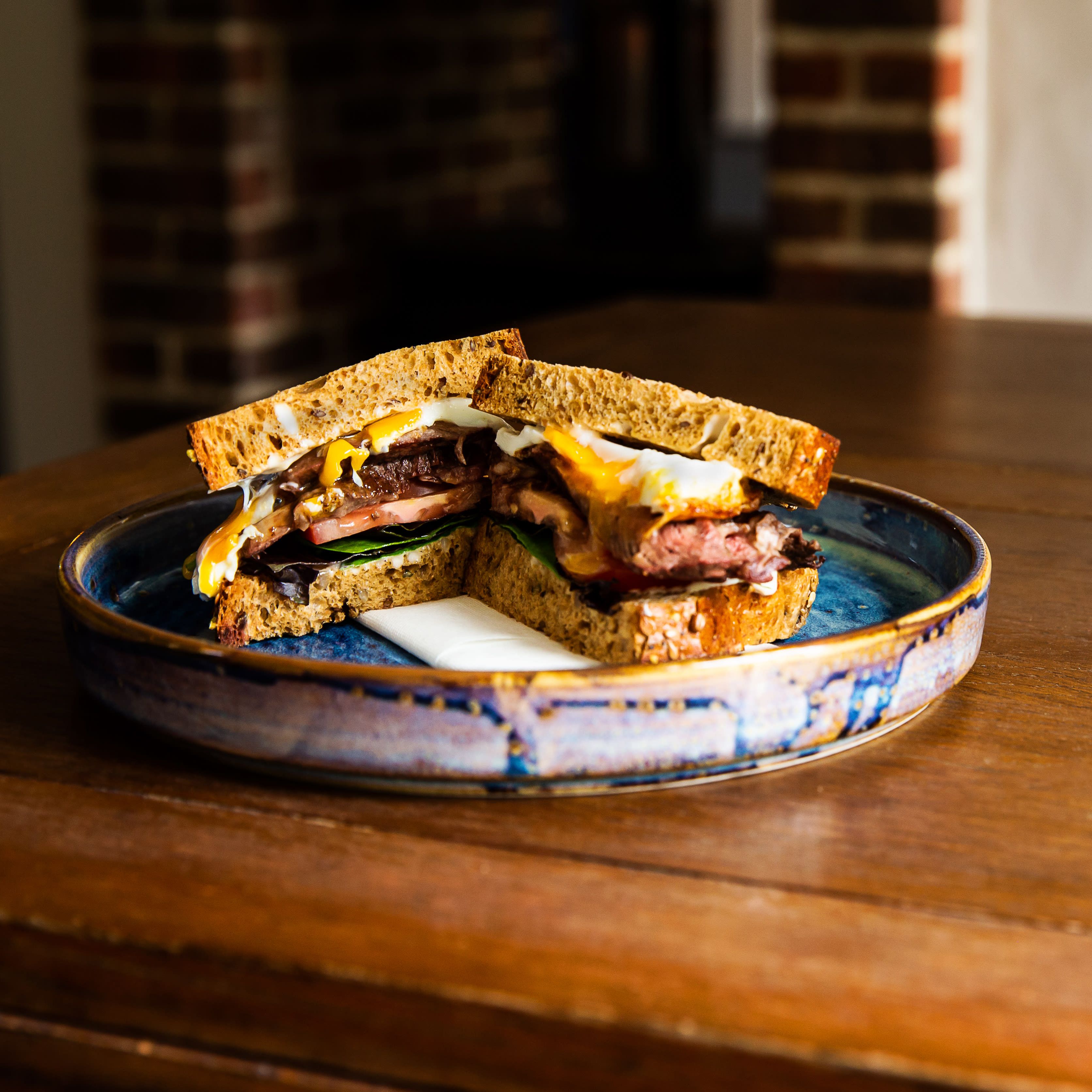 A hearty sandwich with meat, cheese, and egg on whole grain bread, served on a ceramic plate.
