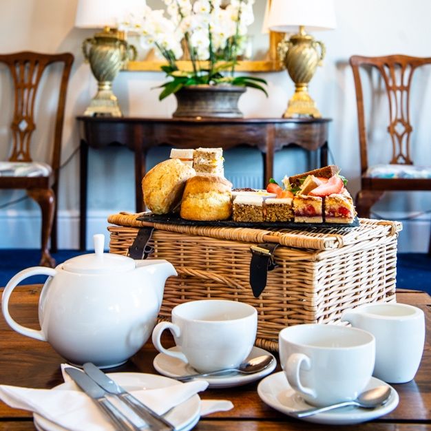 Elegant afternoon tea setting with teapot, cups and pastries on a basket in a luxurious room