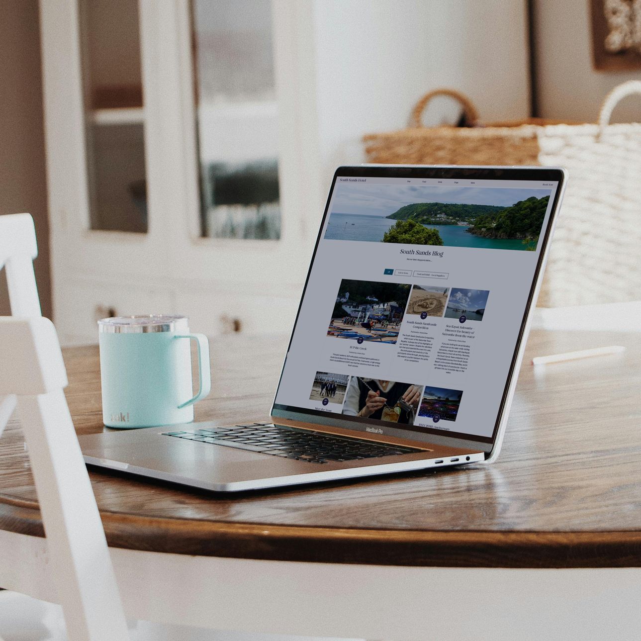 Laptop displaying South Sands Blog on a wooden table with a blue mug beside it