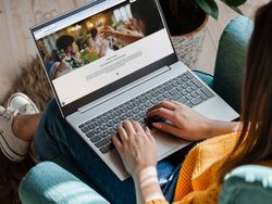 Person using a laptop while sitting on a teal armchair, viewing a website with a celebration theme.